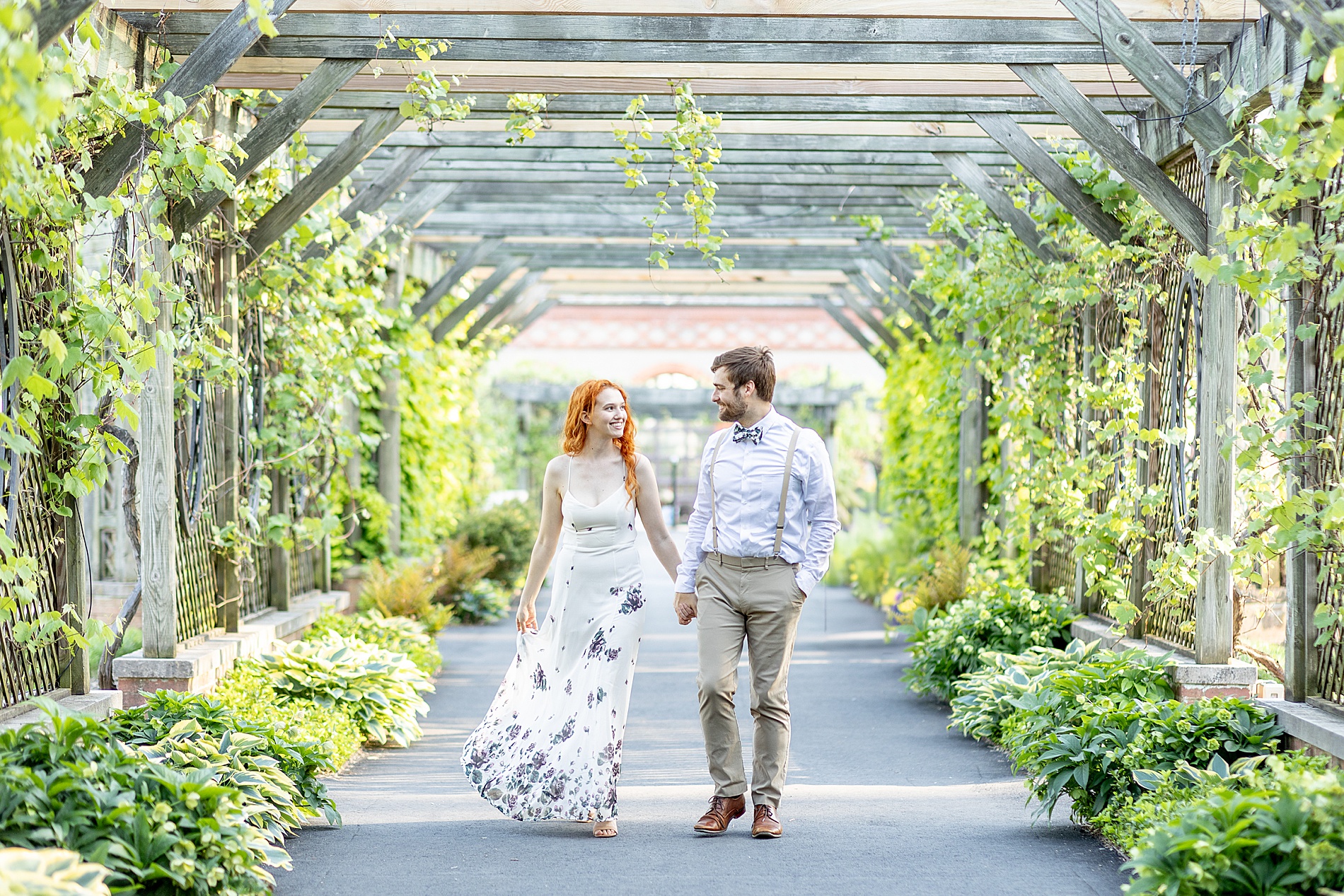 couple walk under archway covered in greenery