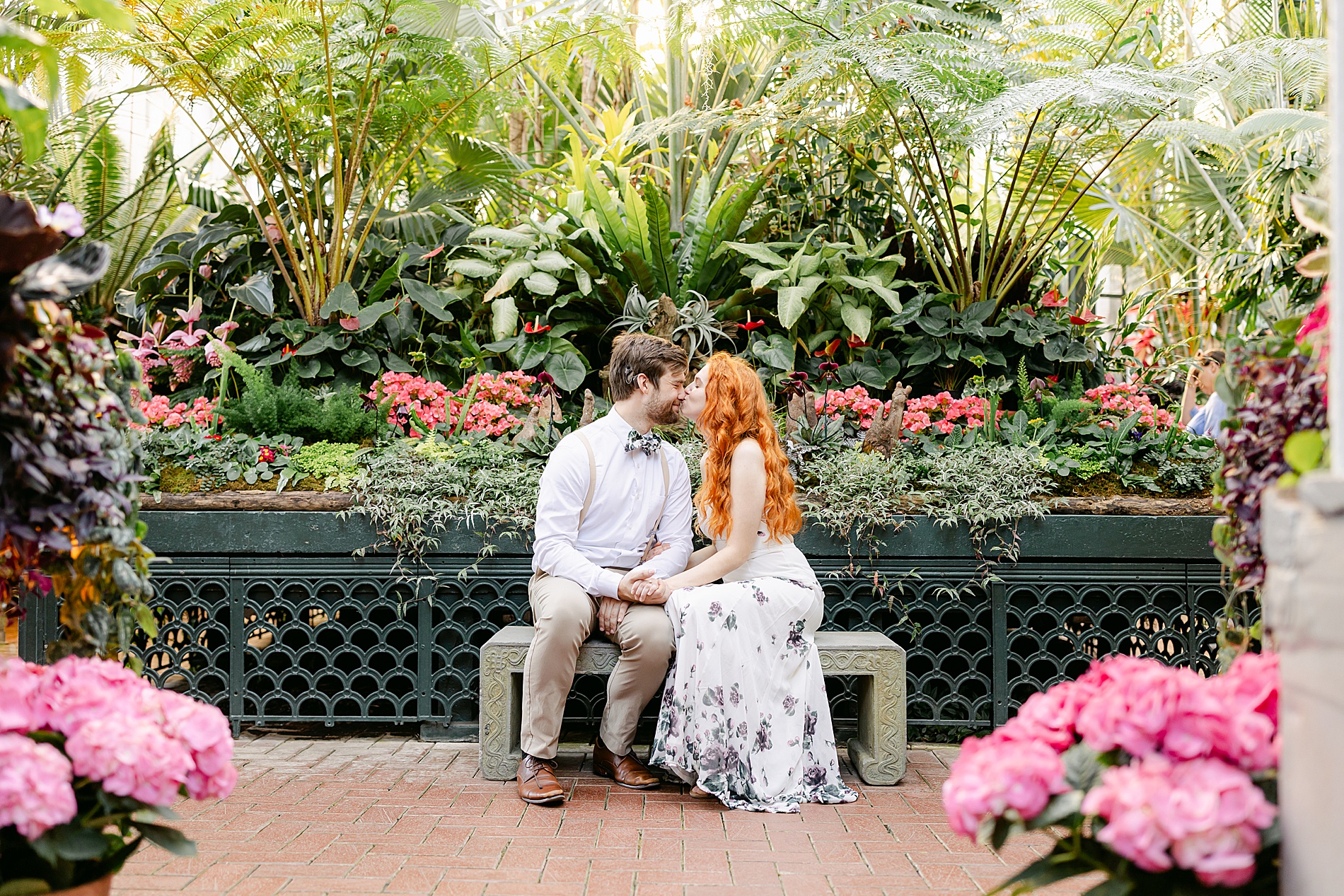 couple kiss on bench inside beautiful conservatory 