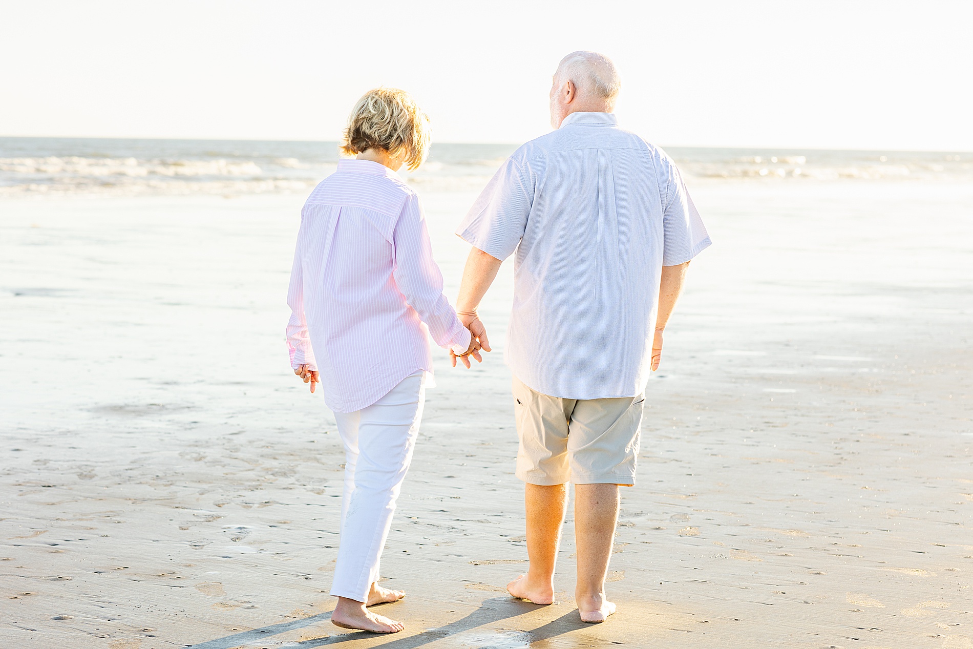 husband and wife hold hands as they walk along the beach