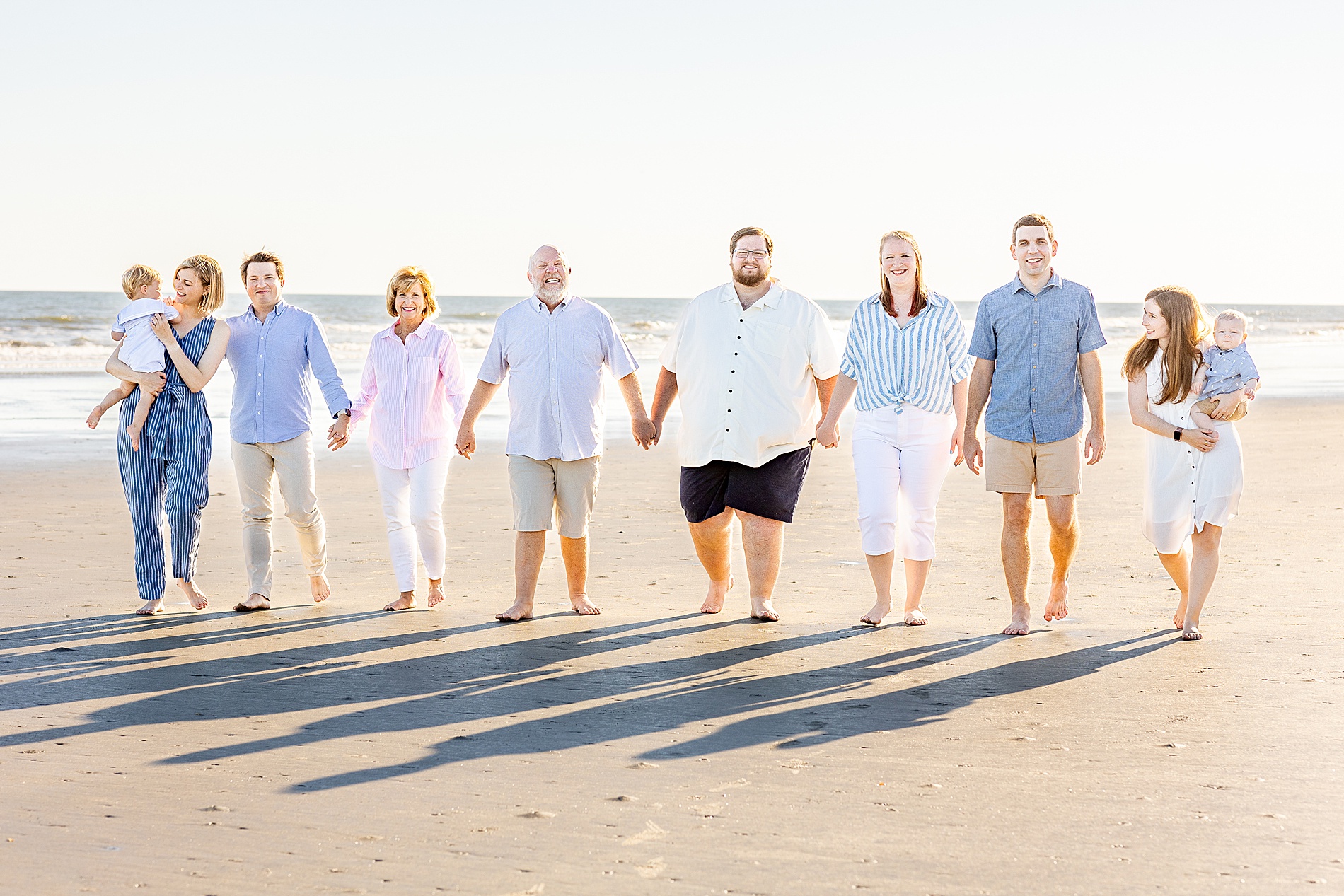 extended family hold hands as they walk the beach