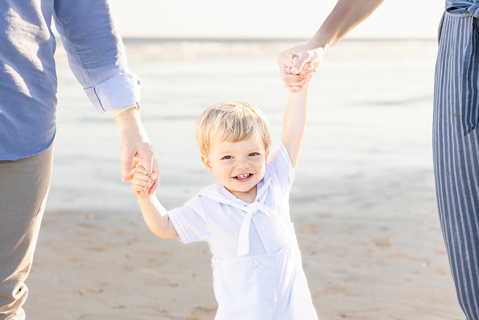 little boy hold his parents' hands on the beach in Charleston