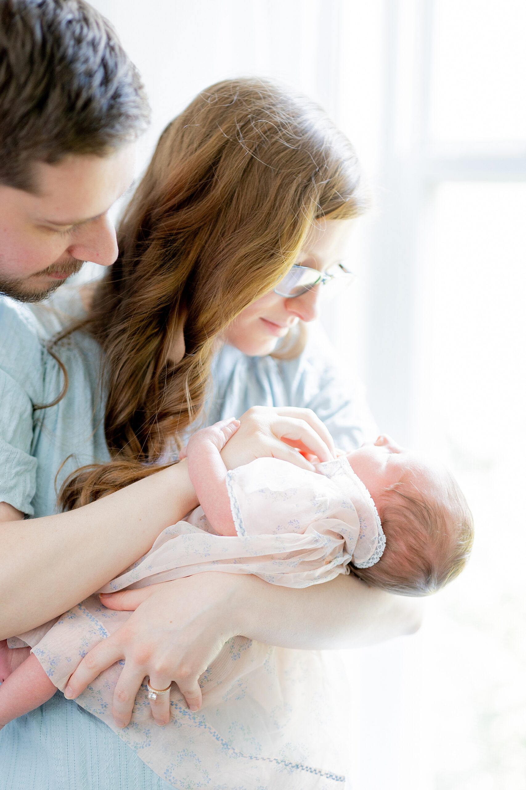 parents hold baby girl by window 