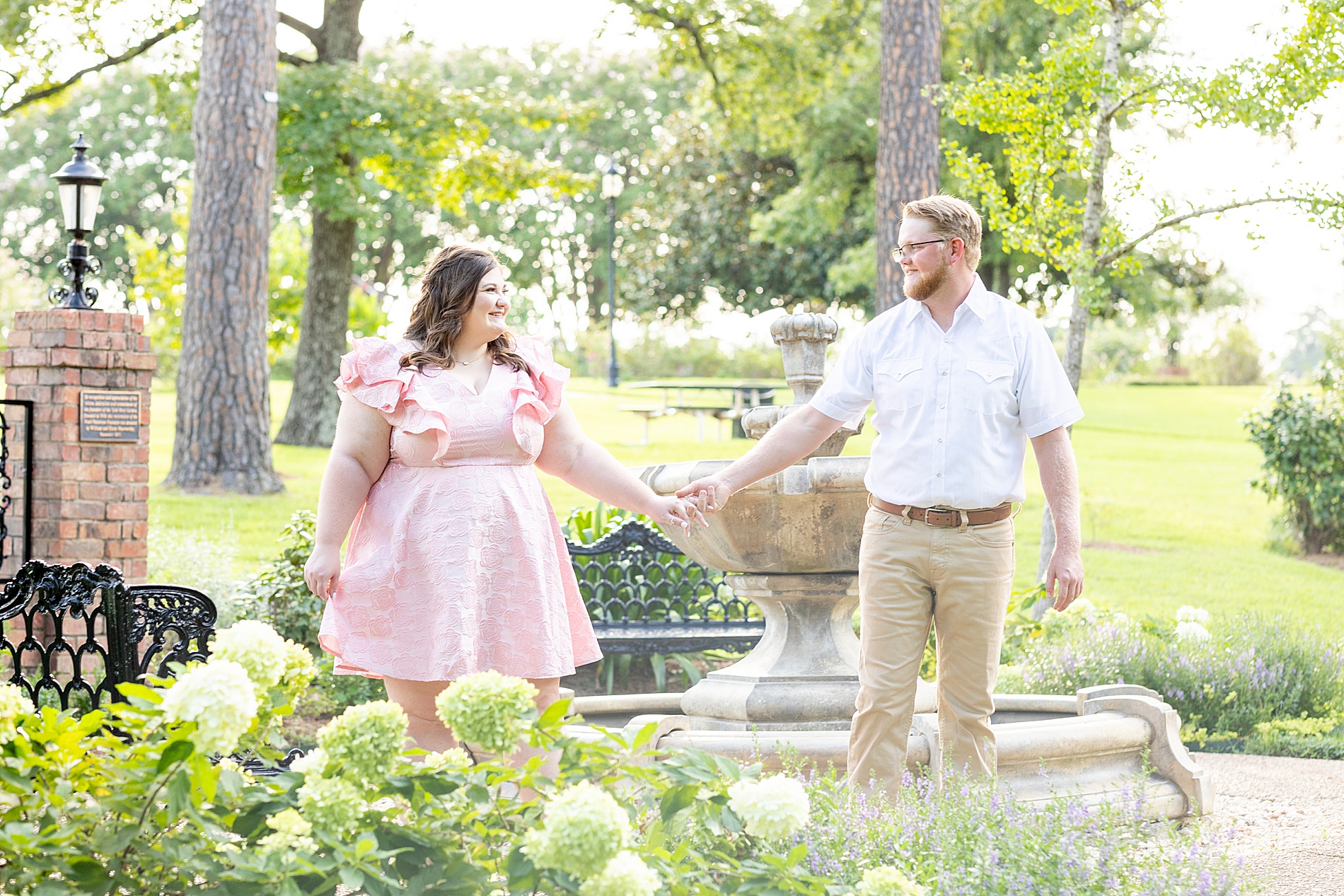 engaged couple hold hands as they walk through Tyler Rose Garden