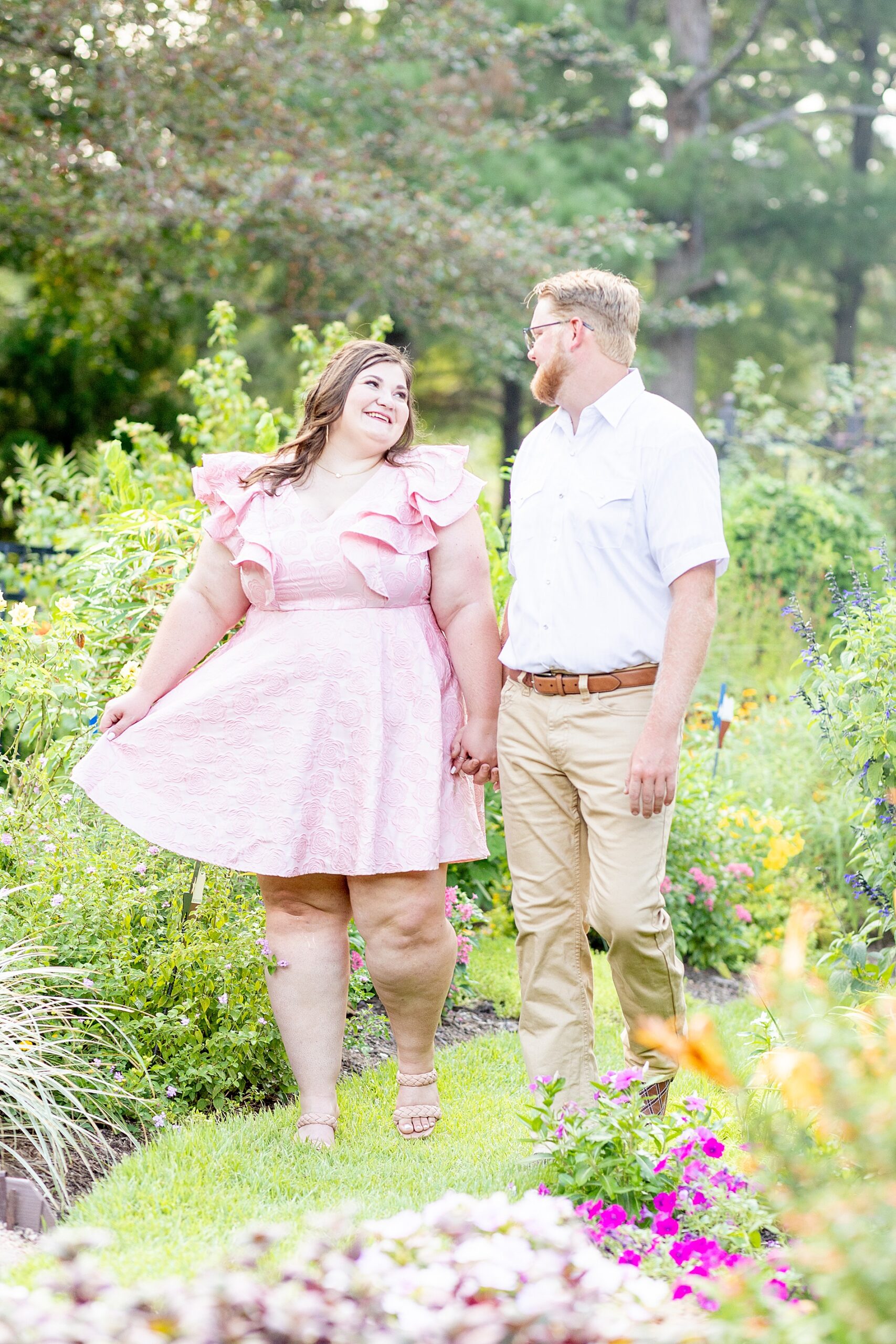 engaged couple hold hands as they walk through garden