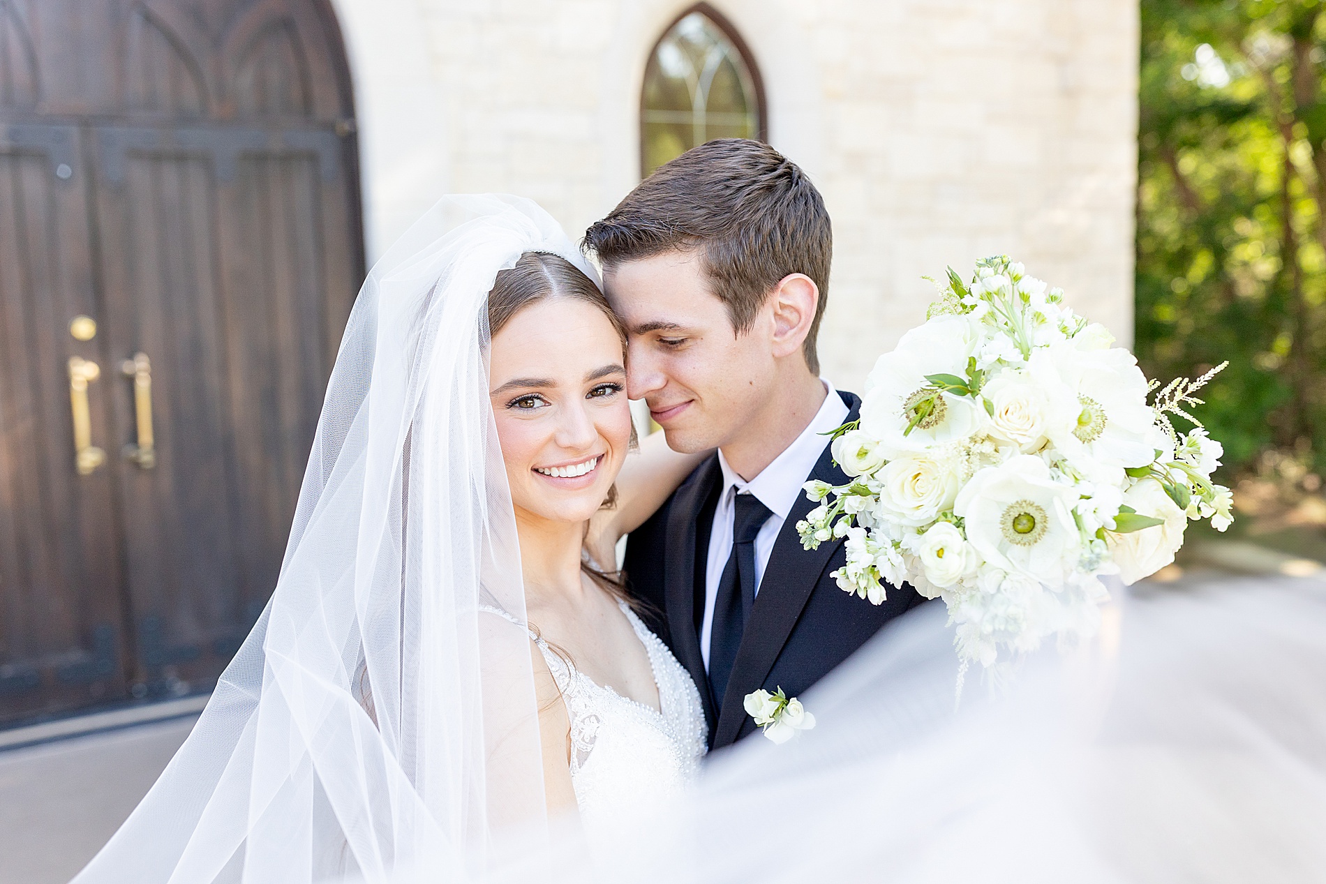 couple outside of chapel with bride's veil surrounding couple