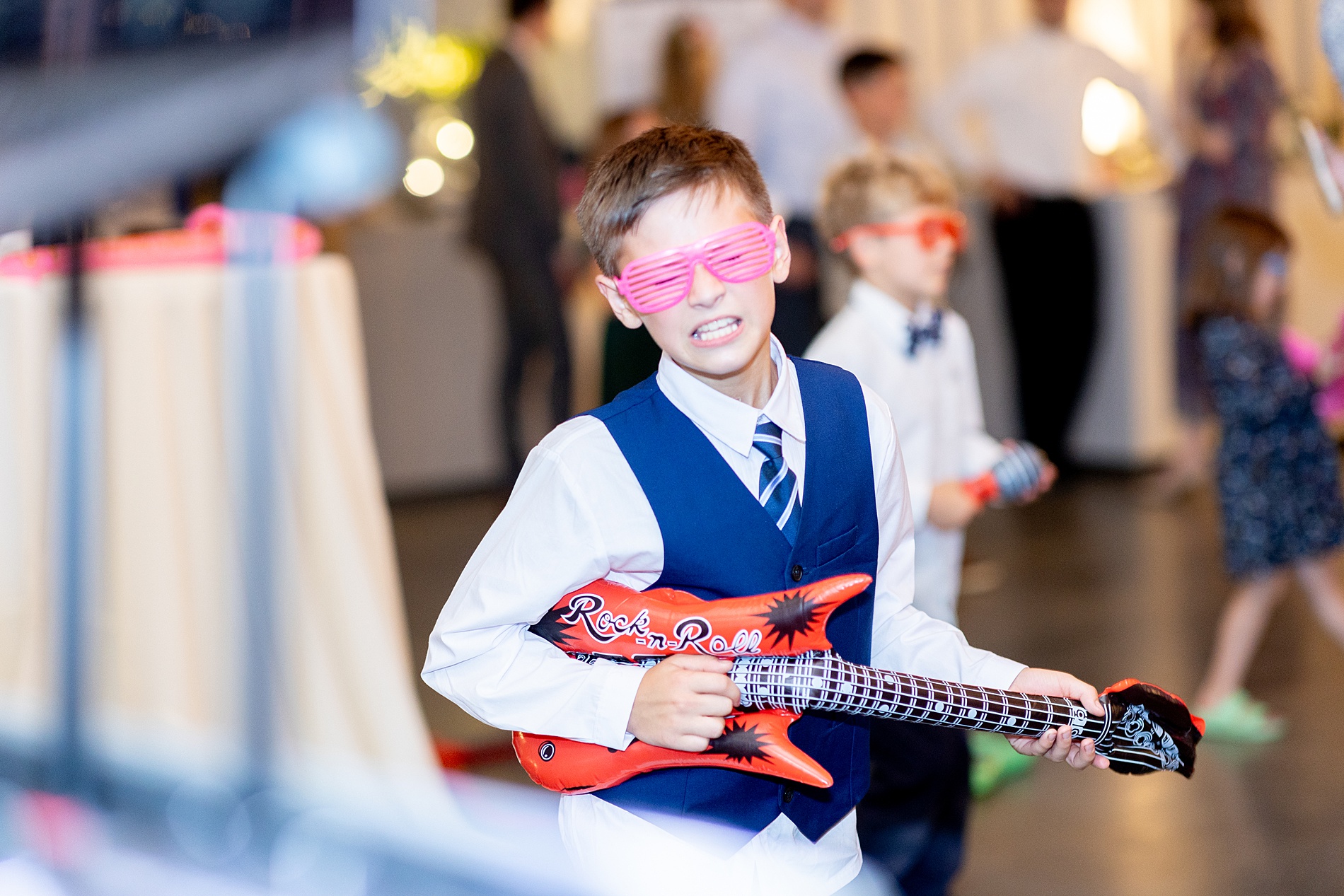 little boy with inflatable guitar and sunglasses at wedding reception