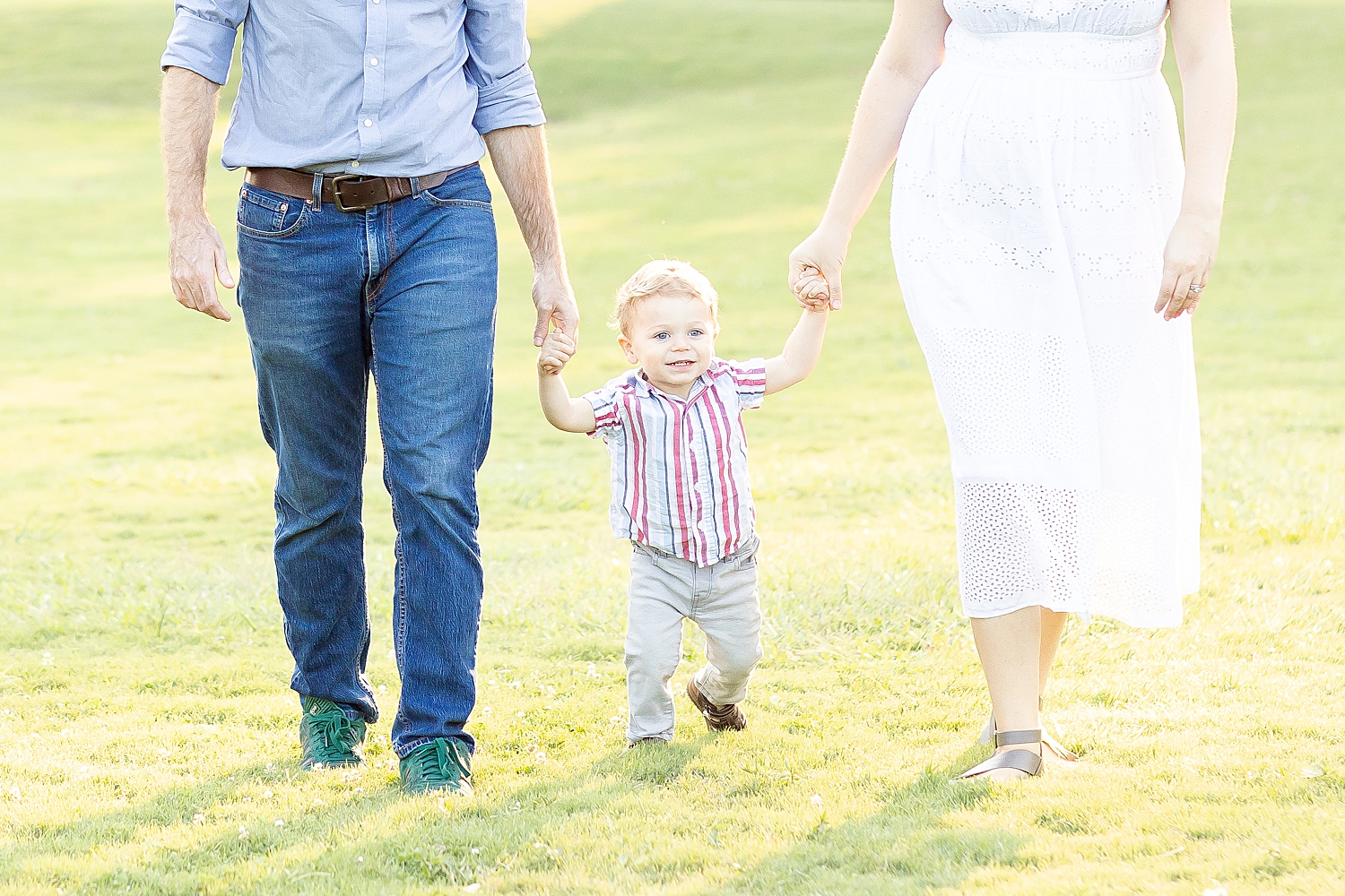 little boy walks holding parent's hands