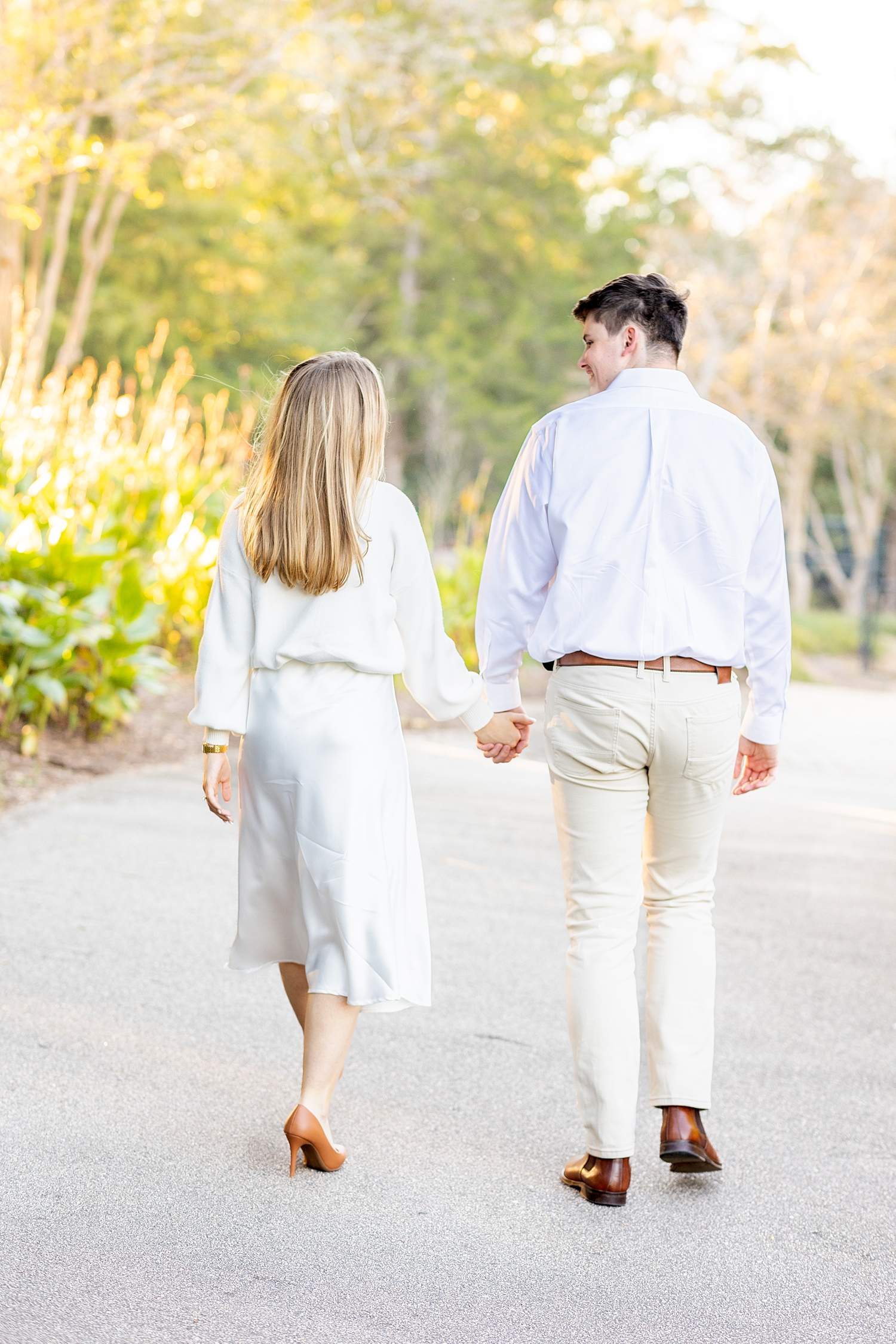 newly engaged couple hold hands as they walk through Pullen Park