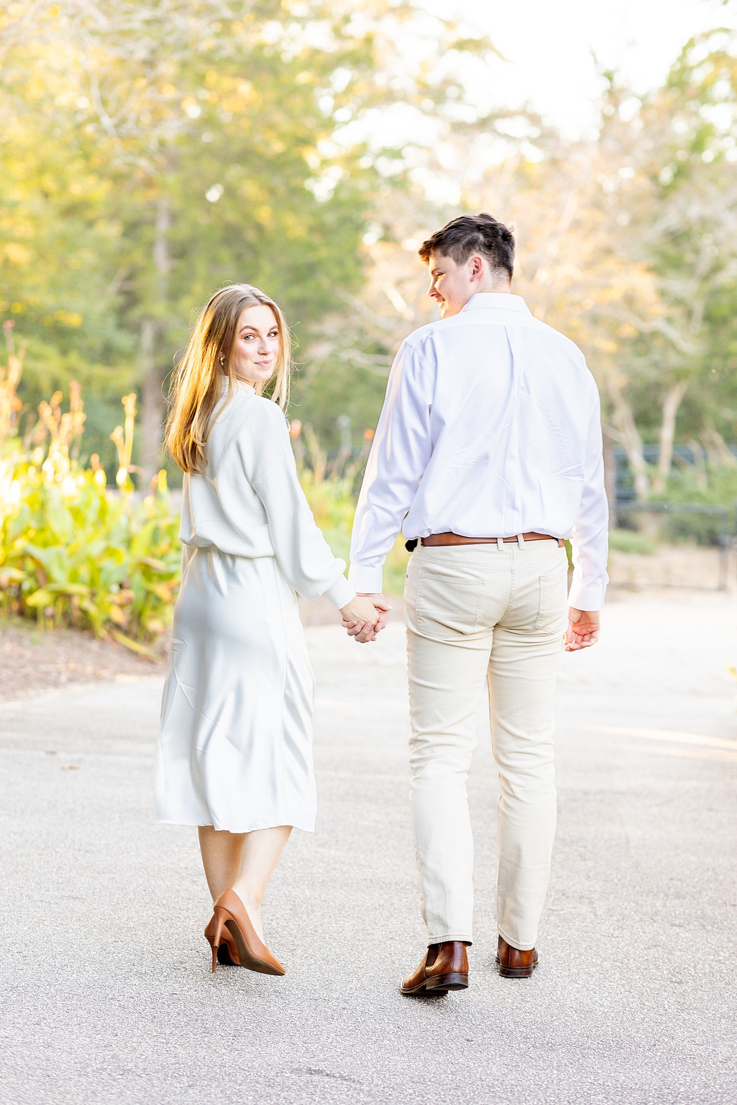 engaged couple hold hands and walk through park in Raleigh, NC