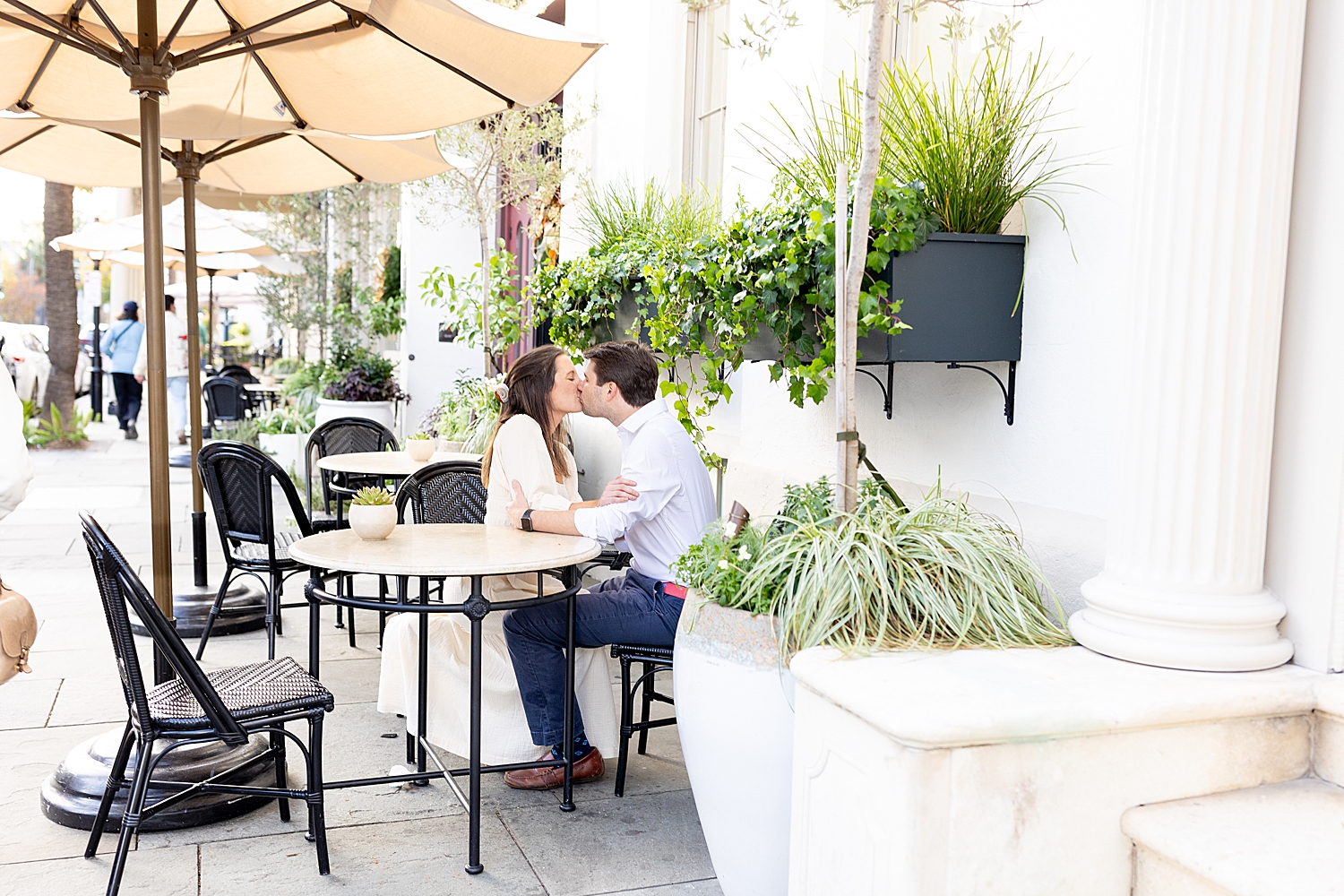 Couple kiss as they sit at table on outdoor patio Romantic Engagement Session 