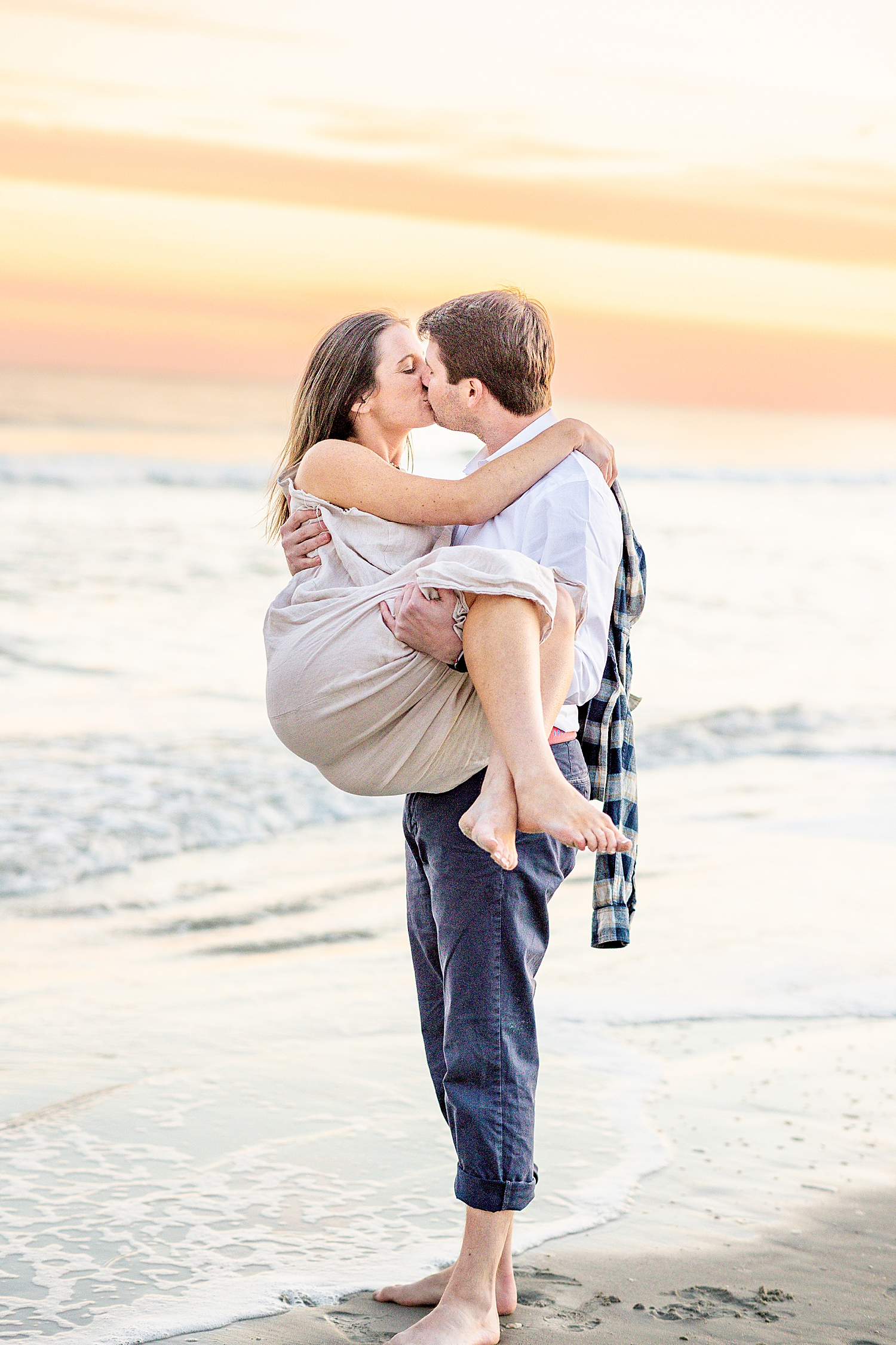 couple kiss as he carries her on the beach