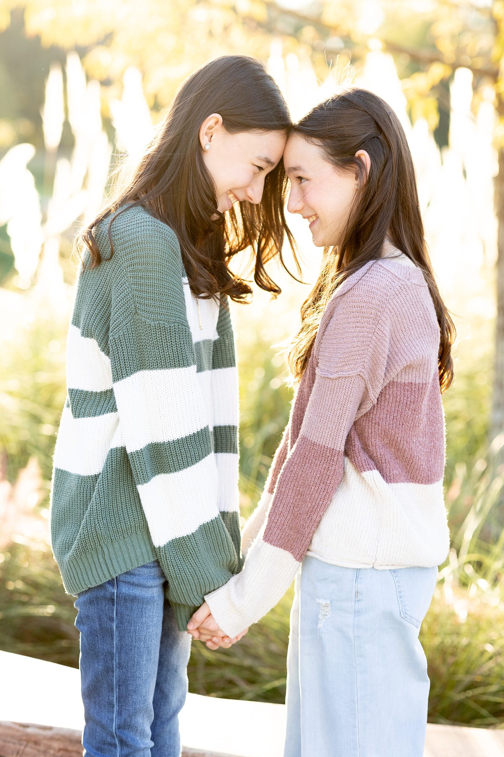 two sisters stand facing each other holding hands