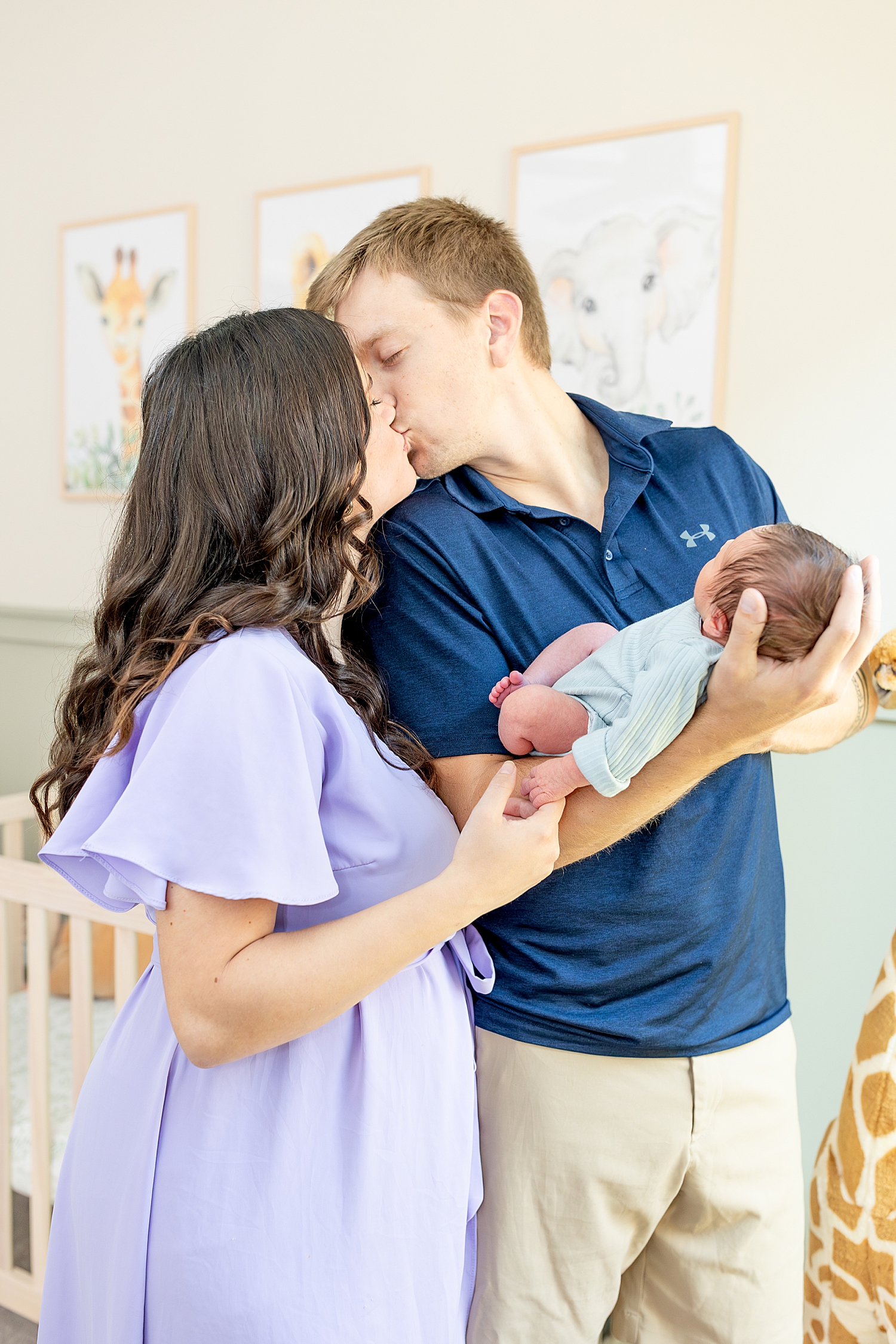 parents kiss as they hold newborn