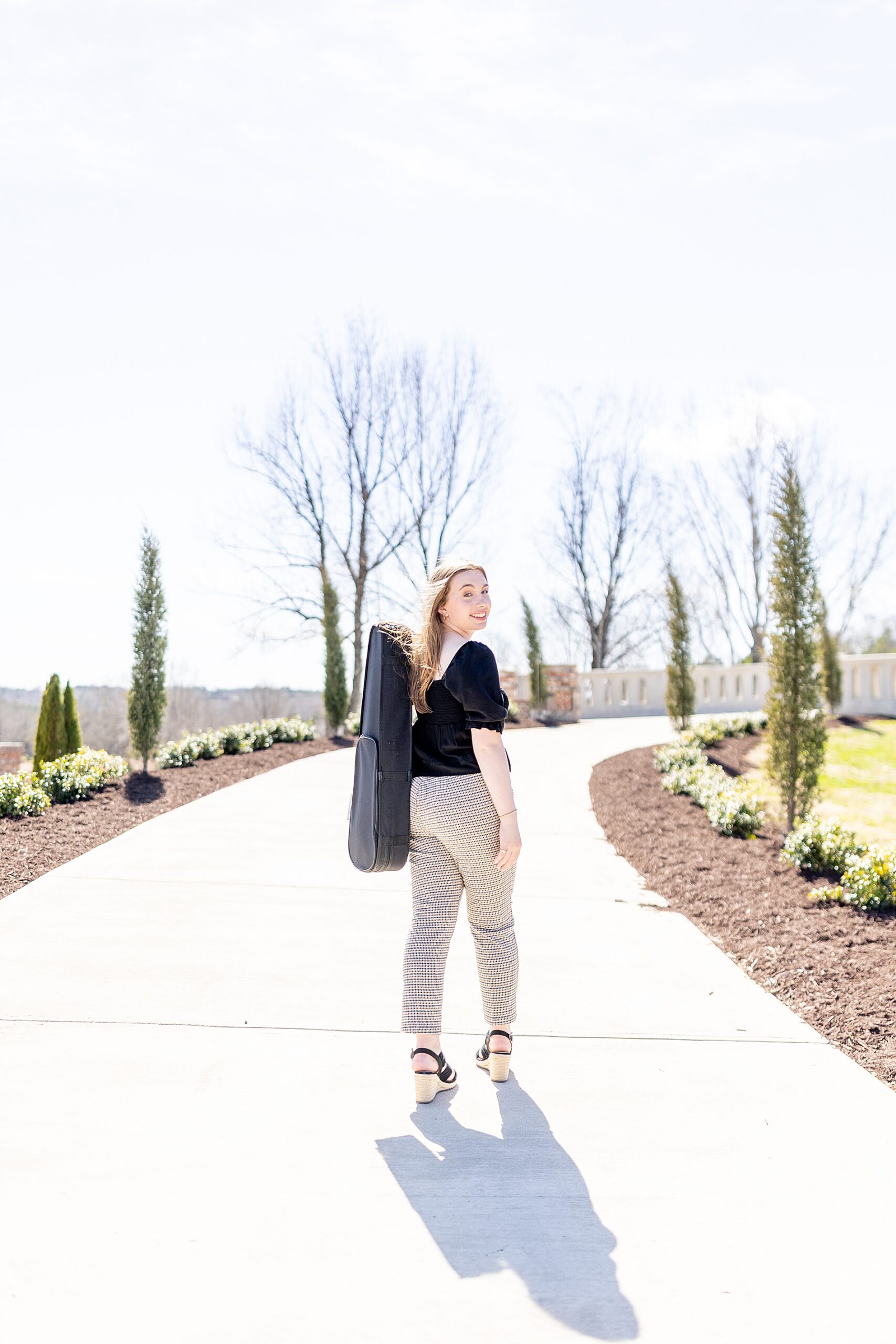 senior walks down sidewalk holding violin case