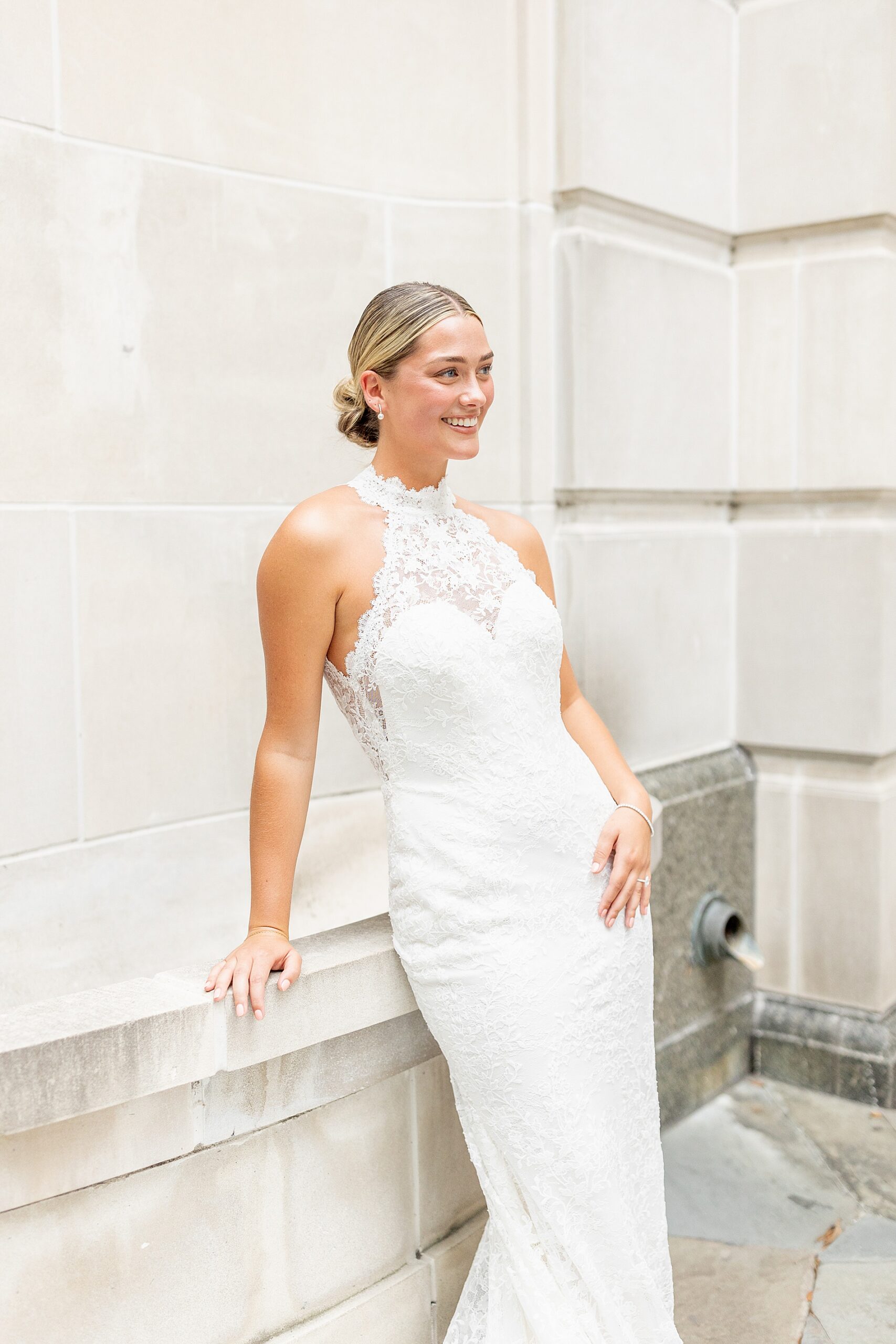 Bride in high neck lace wedding gown leans against stone wall