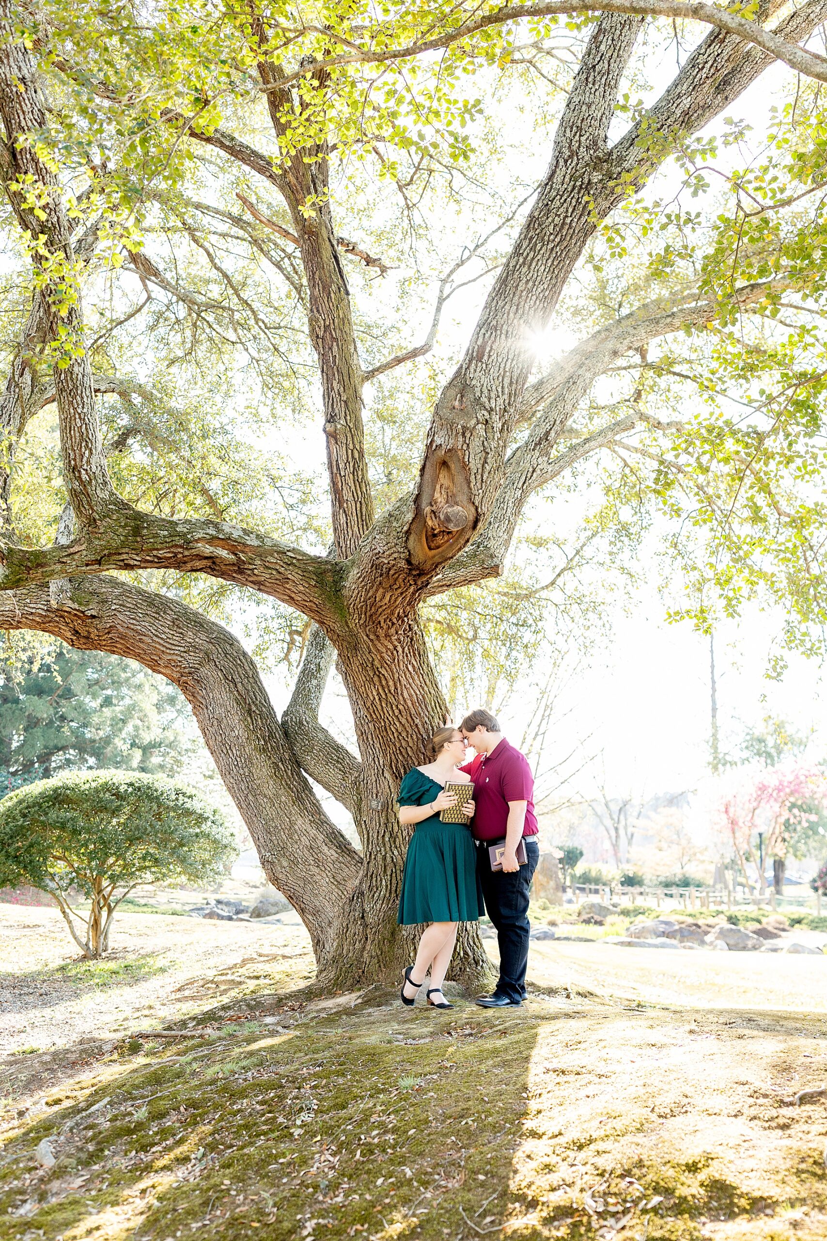 couple lean against oak tree holding books