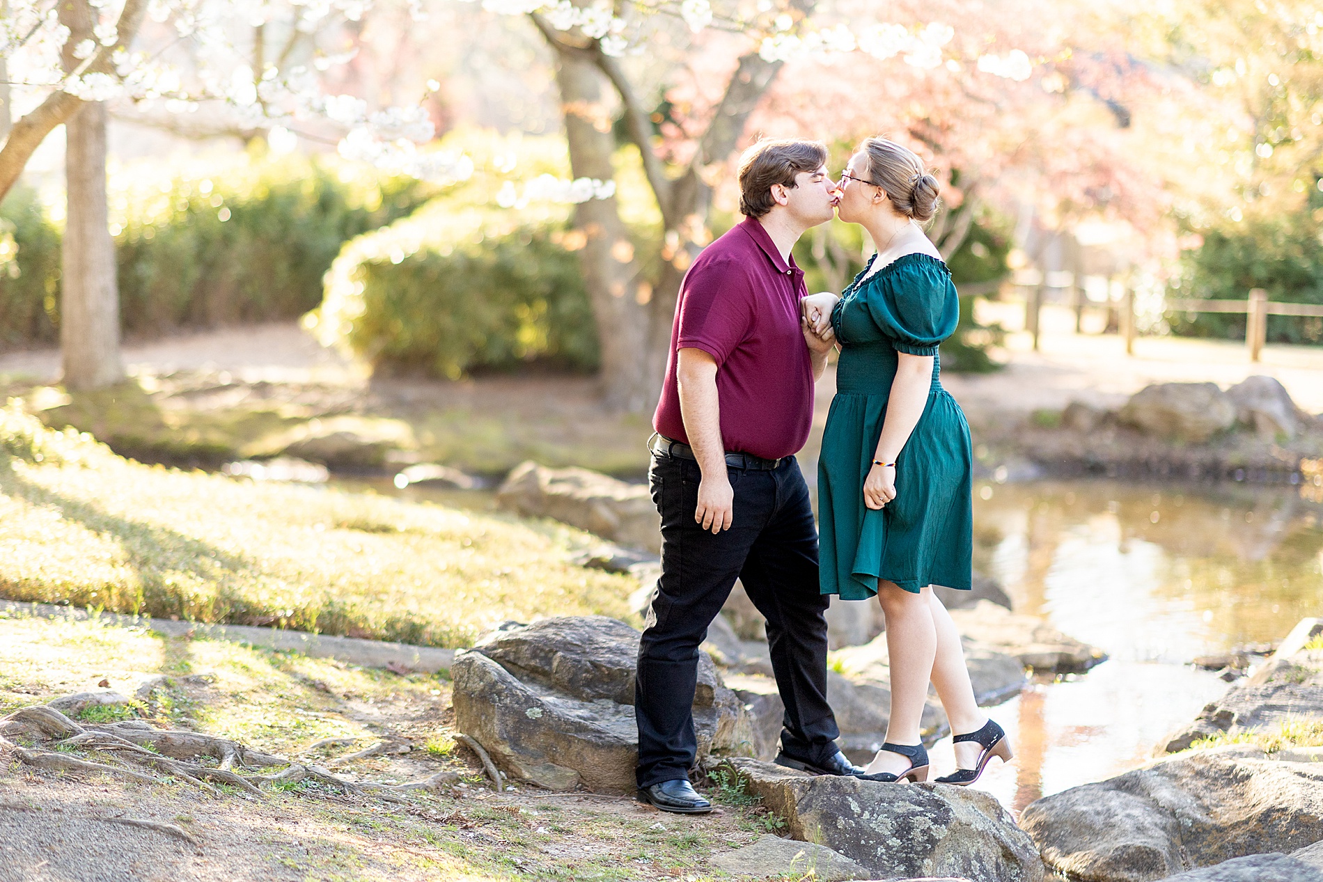 couple kiss while standing on rocks by water