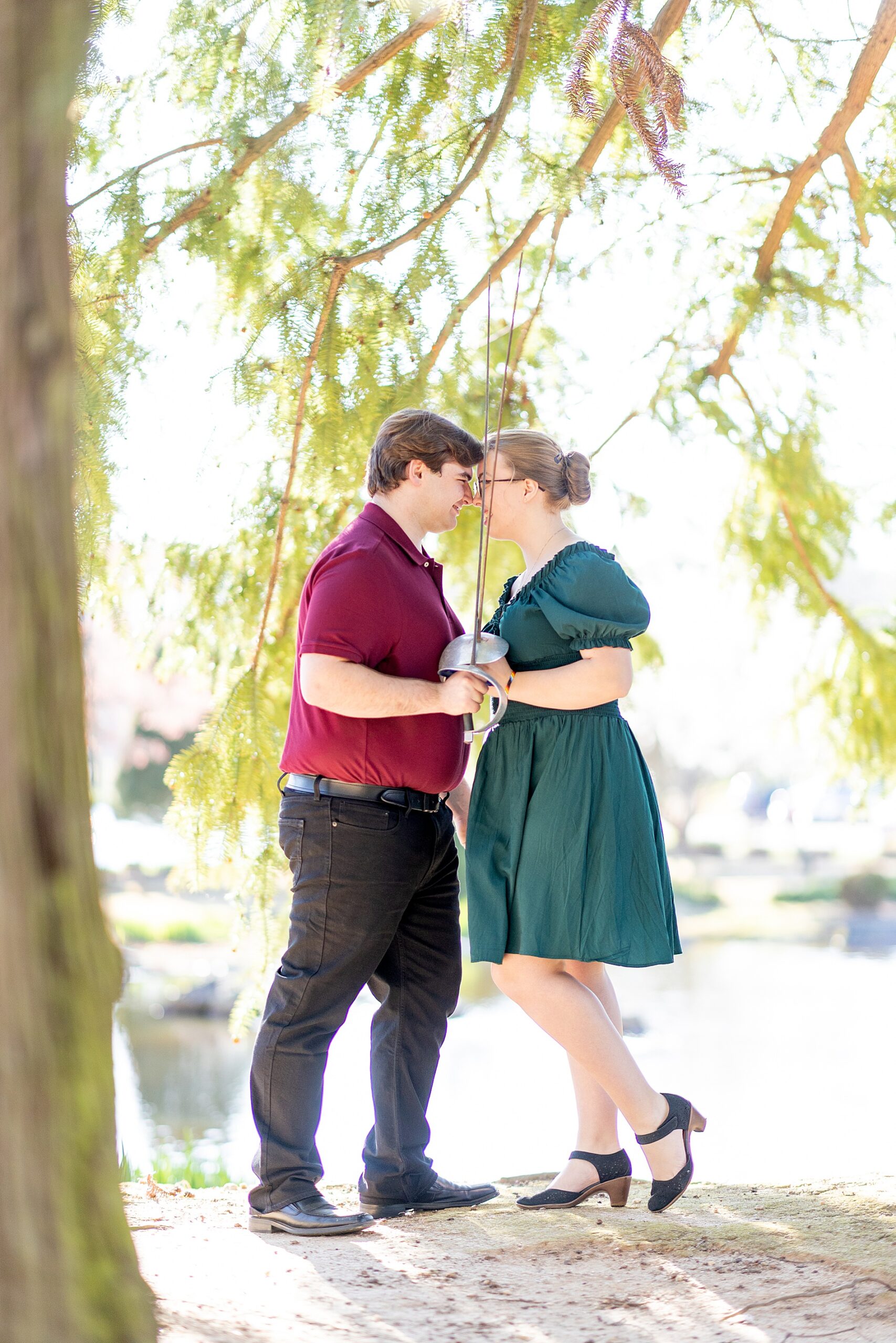couple lean together under tree holding fencing swords