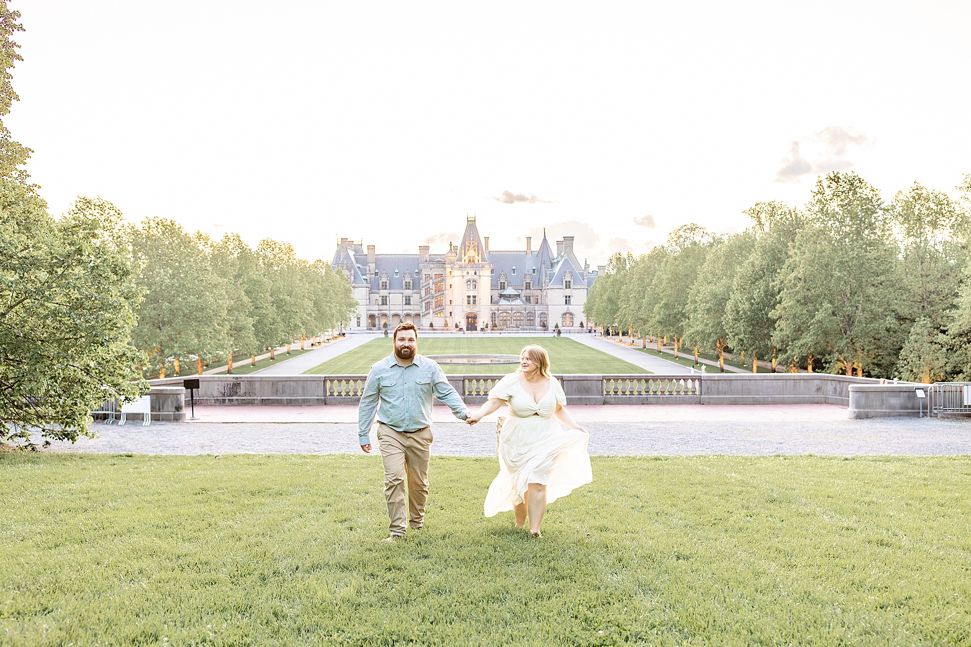 couple hold hands as they walk together on lawn of estate