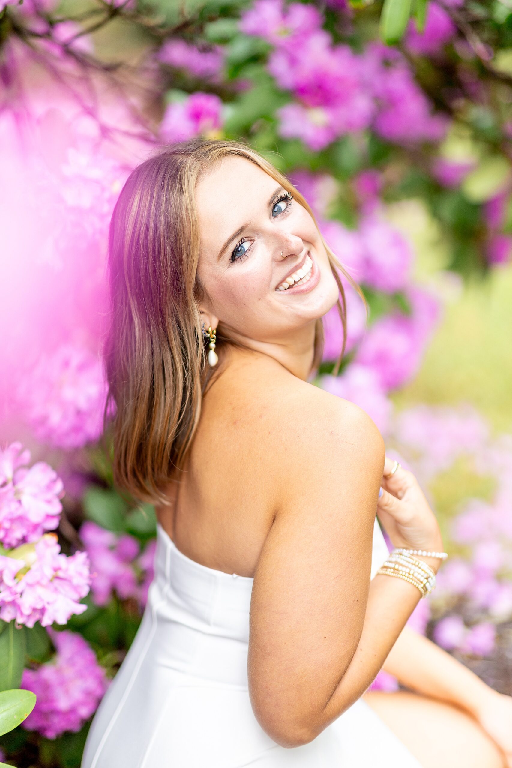 woman smiles over shoulder sitting by pink flowers