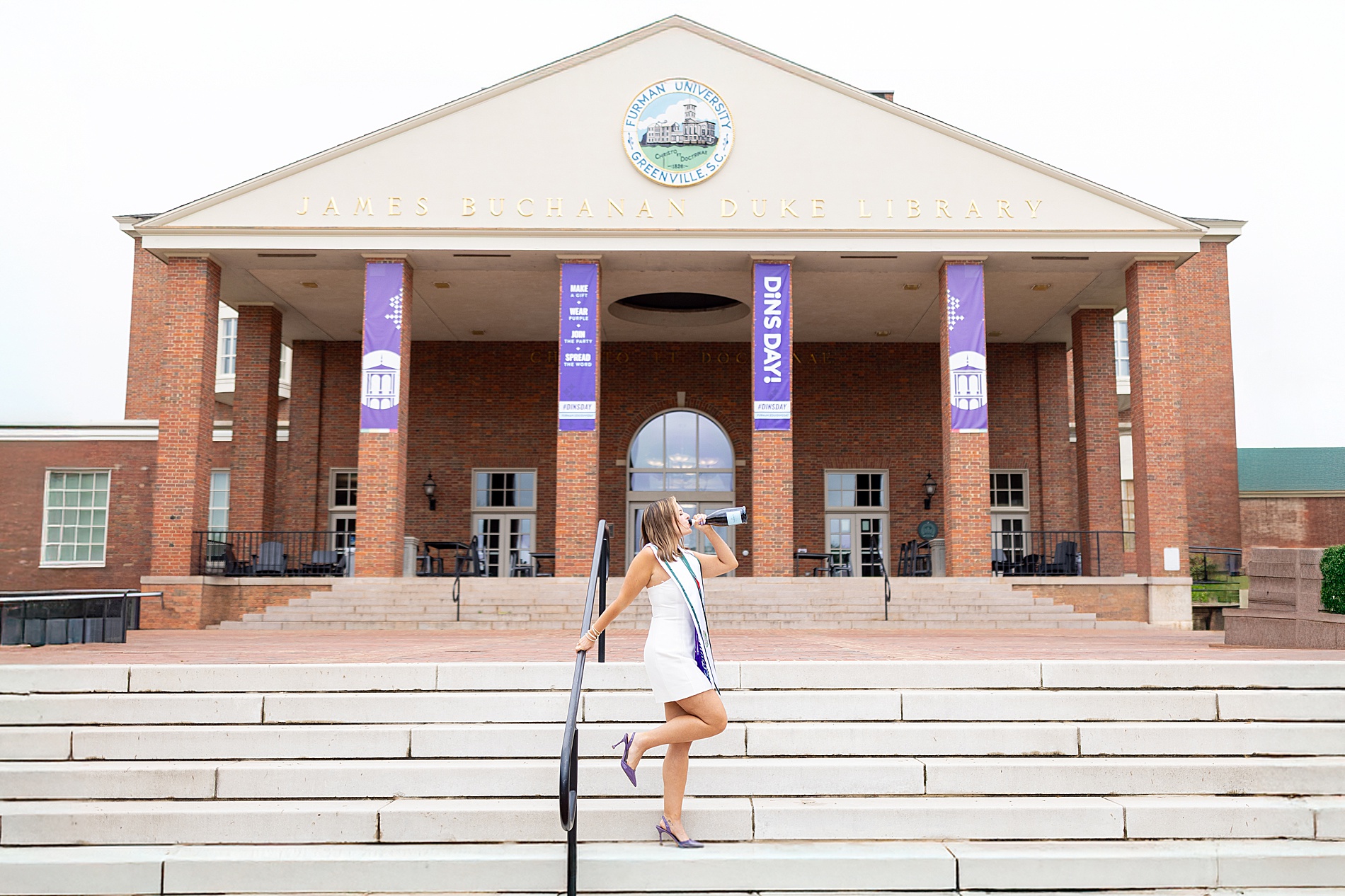 college grad drinks champagne on steps of university building