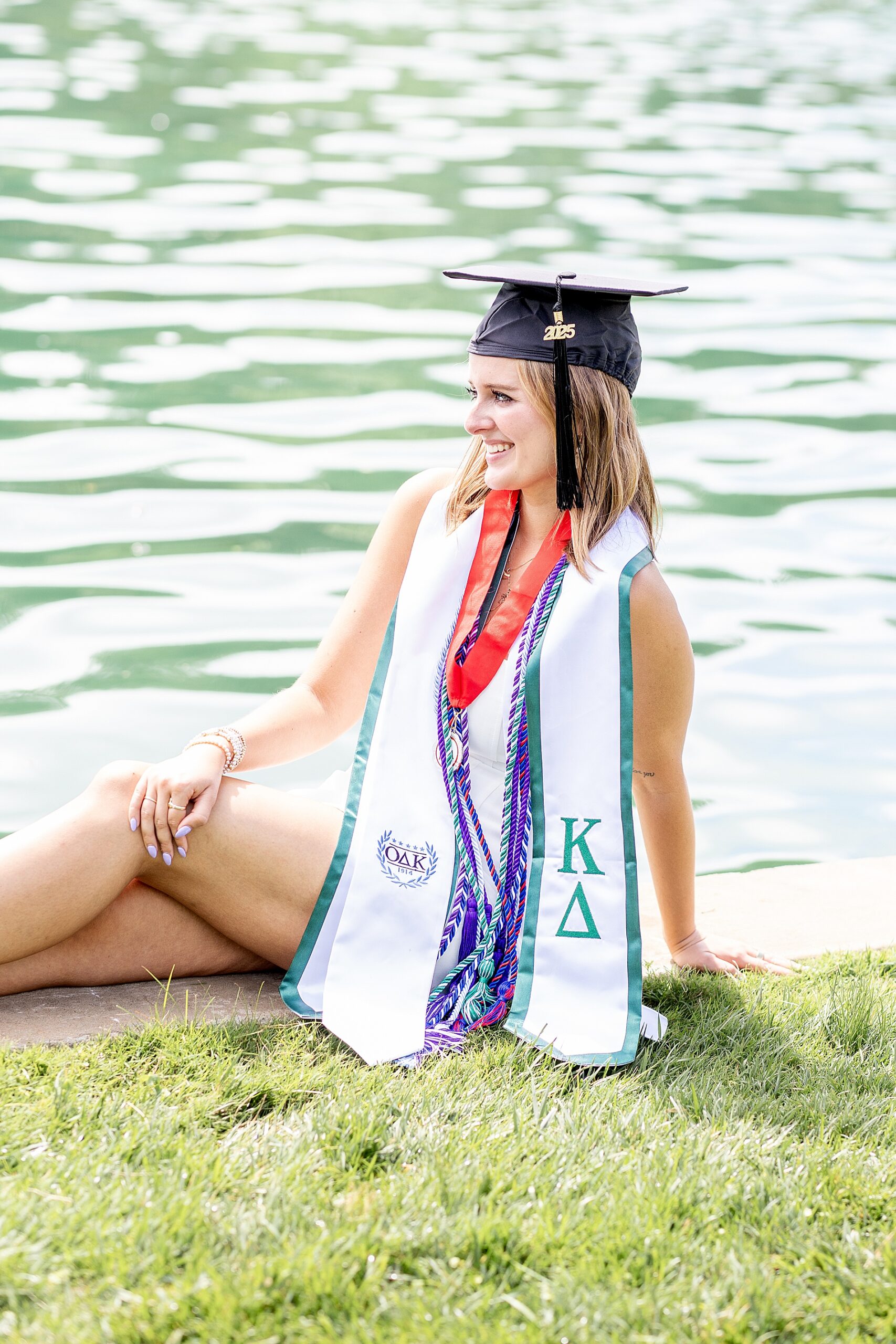 senior sits by the water wearing graduation cap