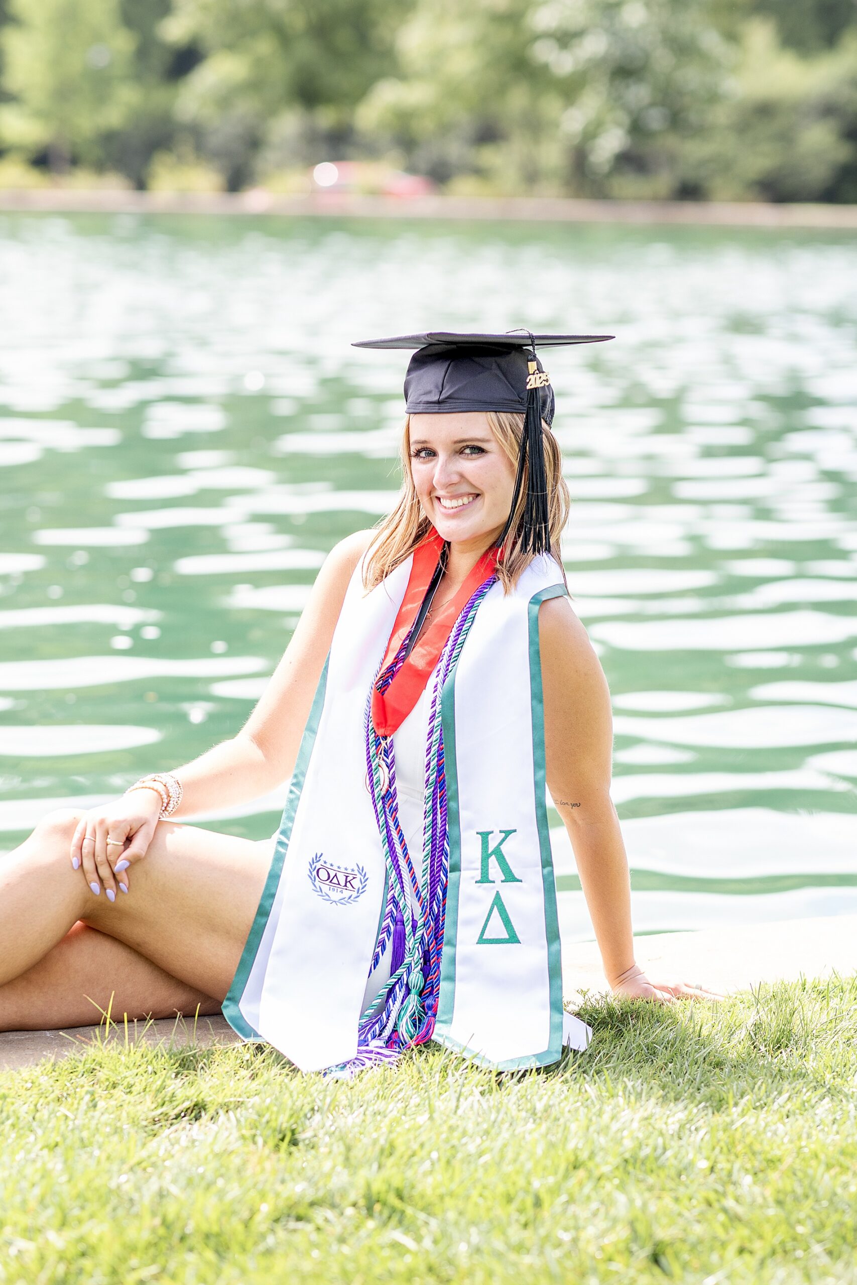 woman sits by water in graduation attire