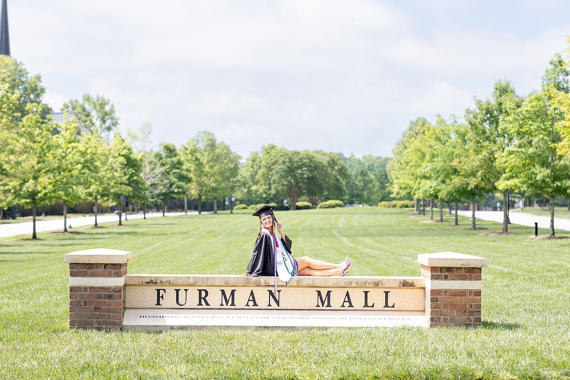 woman sits on Furman Mall sign at Furman University
