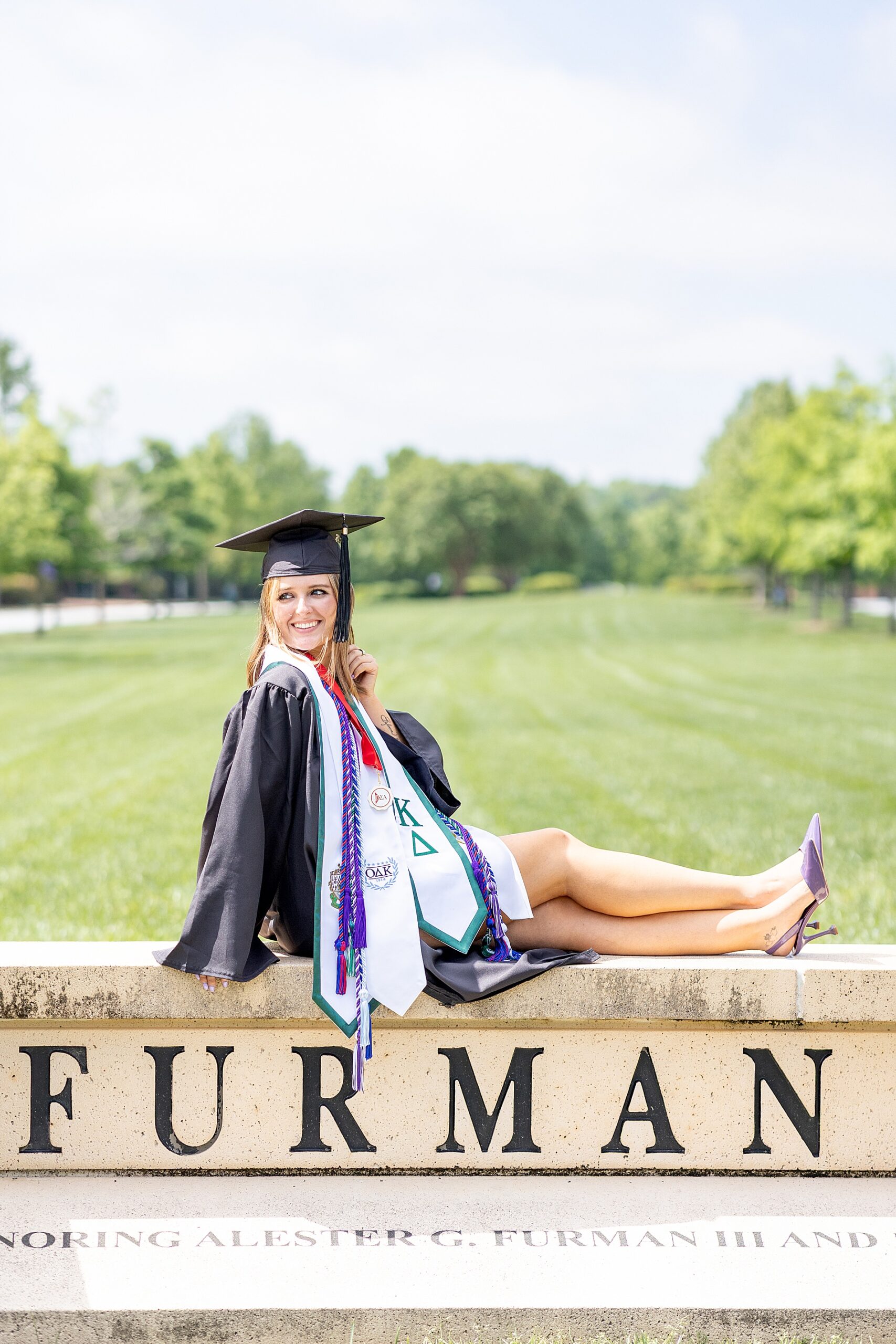 college graduate in cap and gown sits on university sign