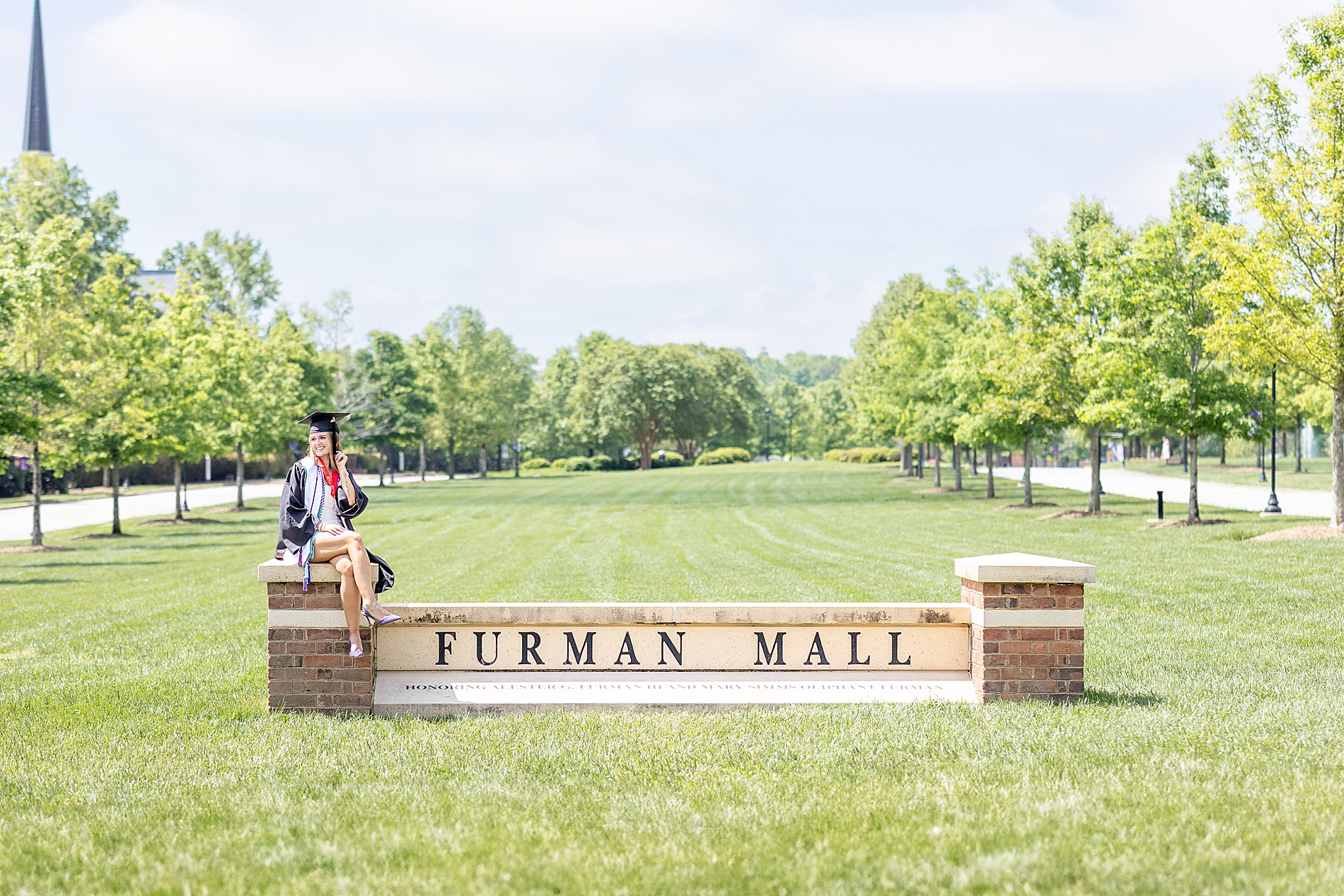 woman sits on brick column of university sign