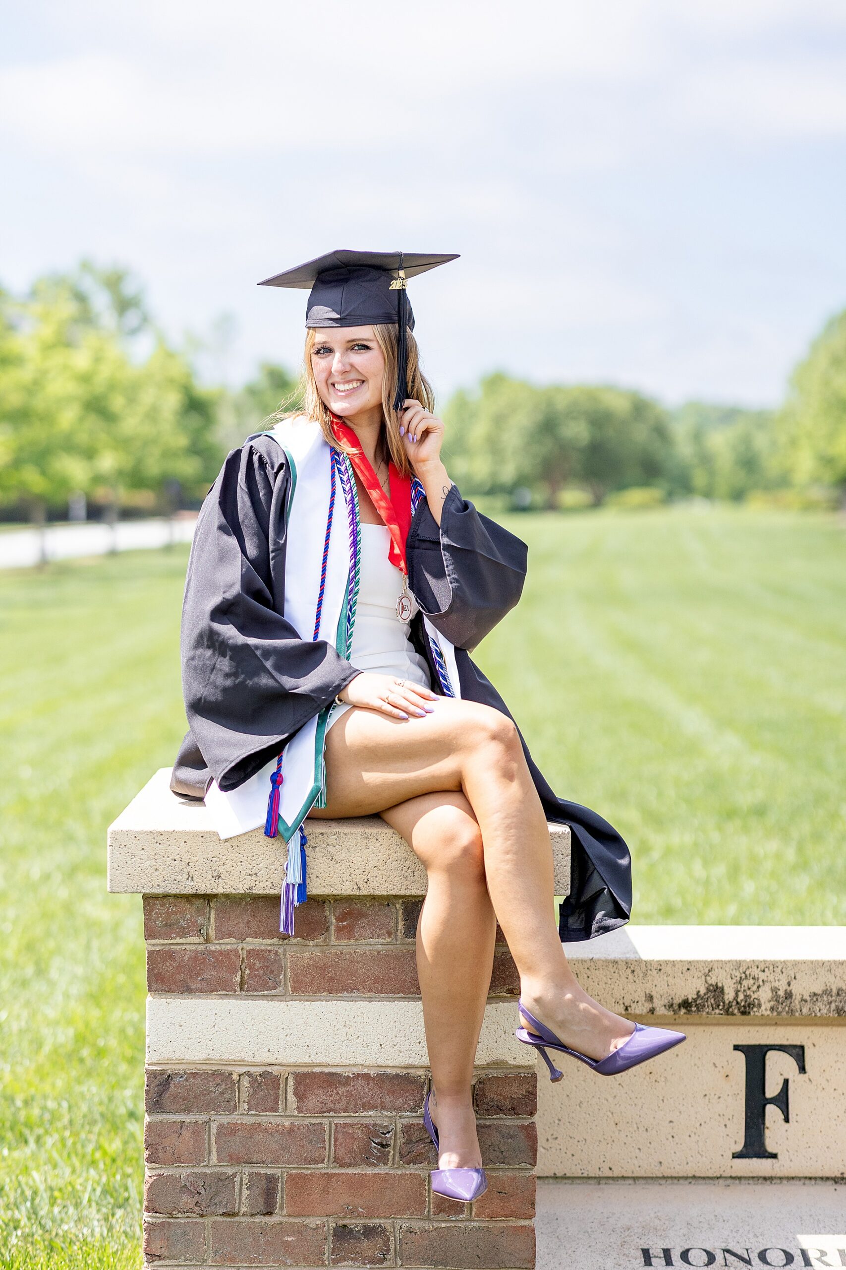 woman sits on brick column of university sign