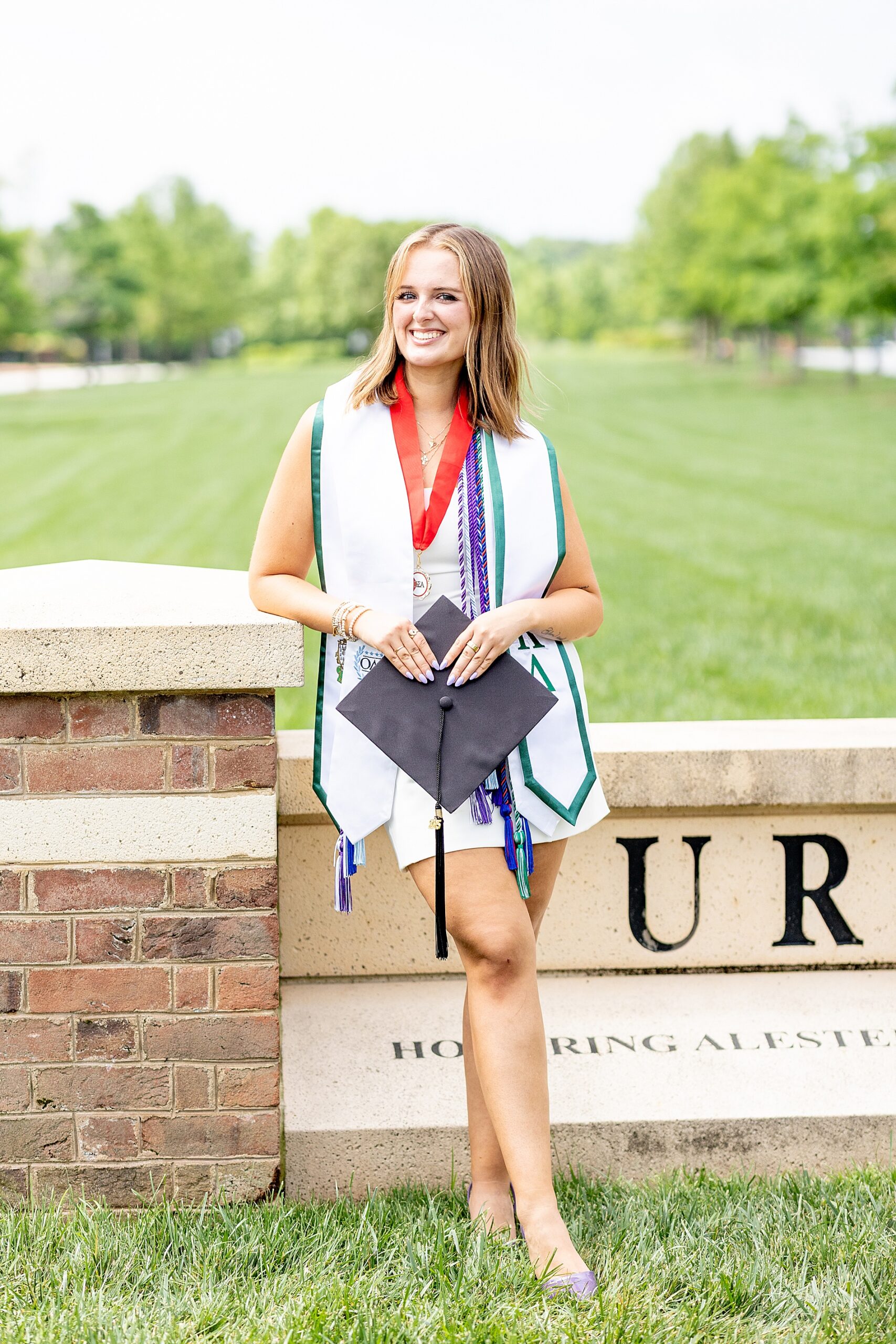 woman in white dress holds graduation cap during grad session