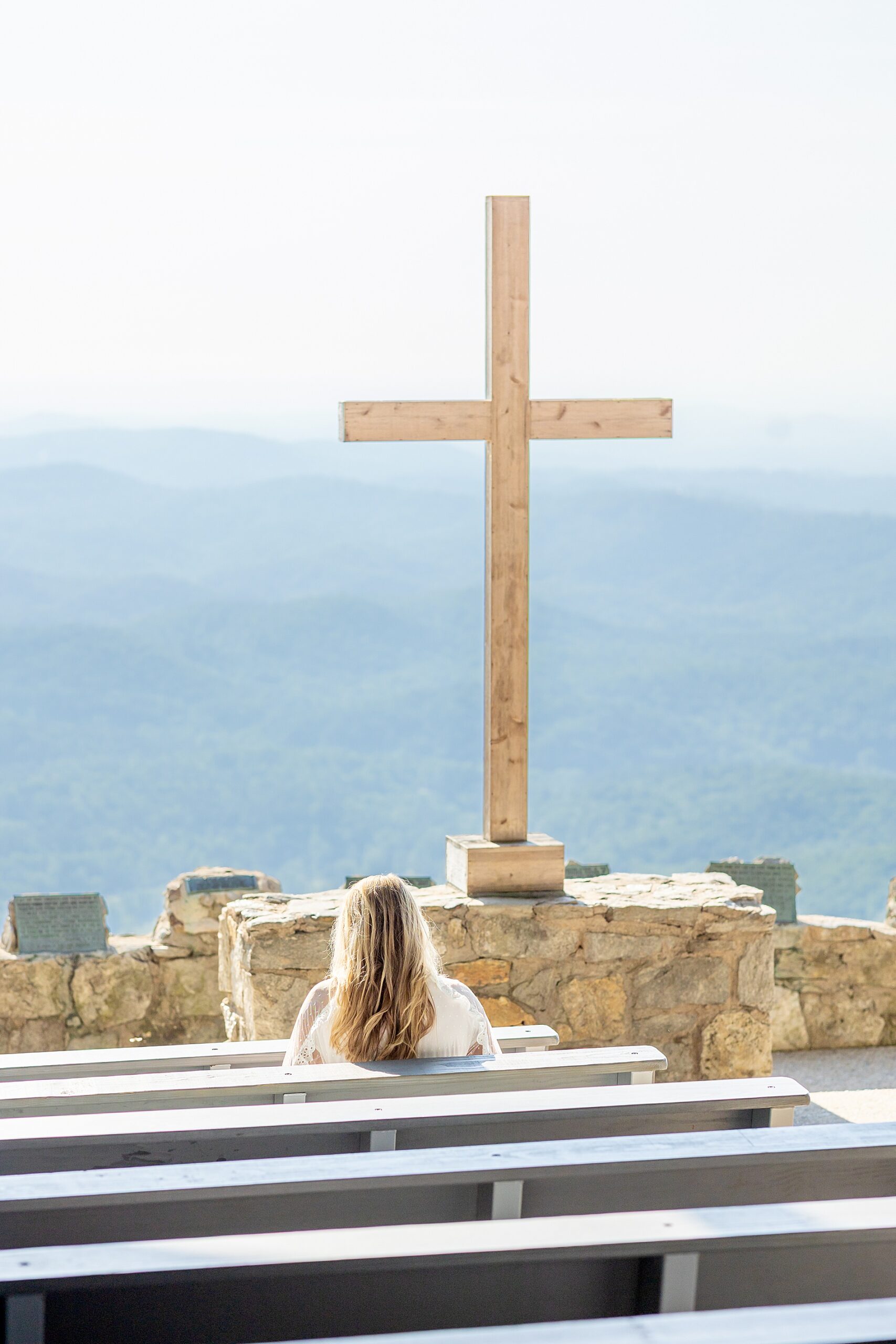 senior girl sits in pew looking at cross and mountain view below