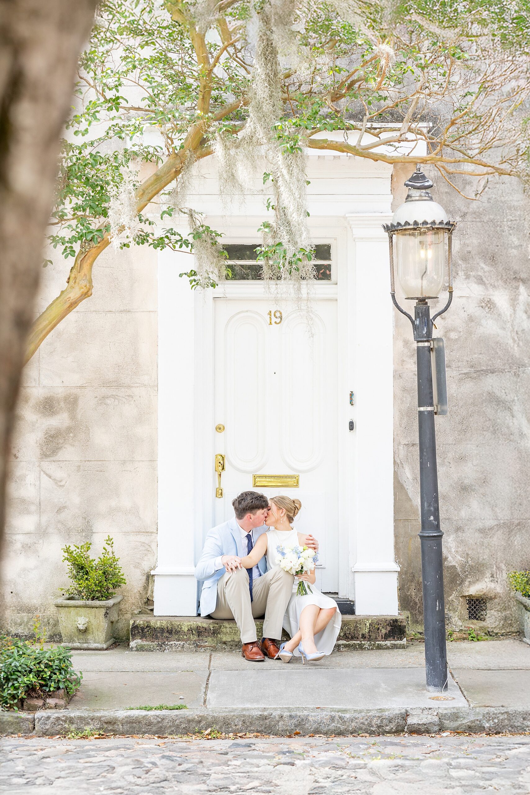 engaged couple kiss as they sit on steps in front of building