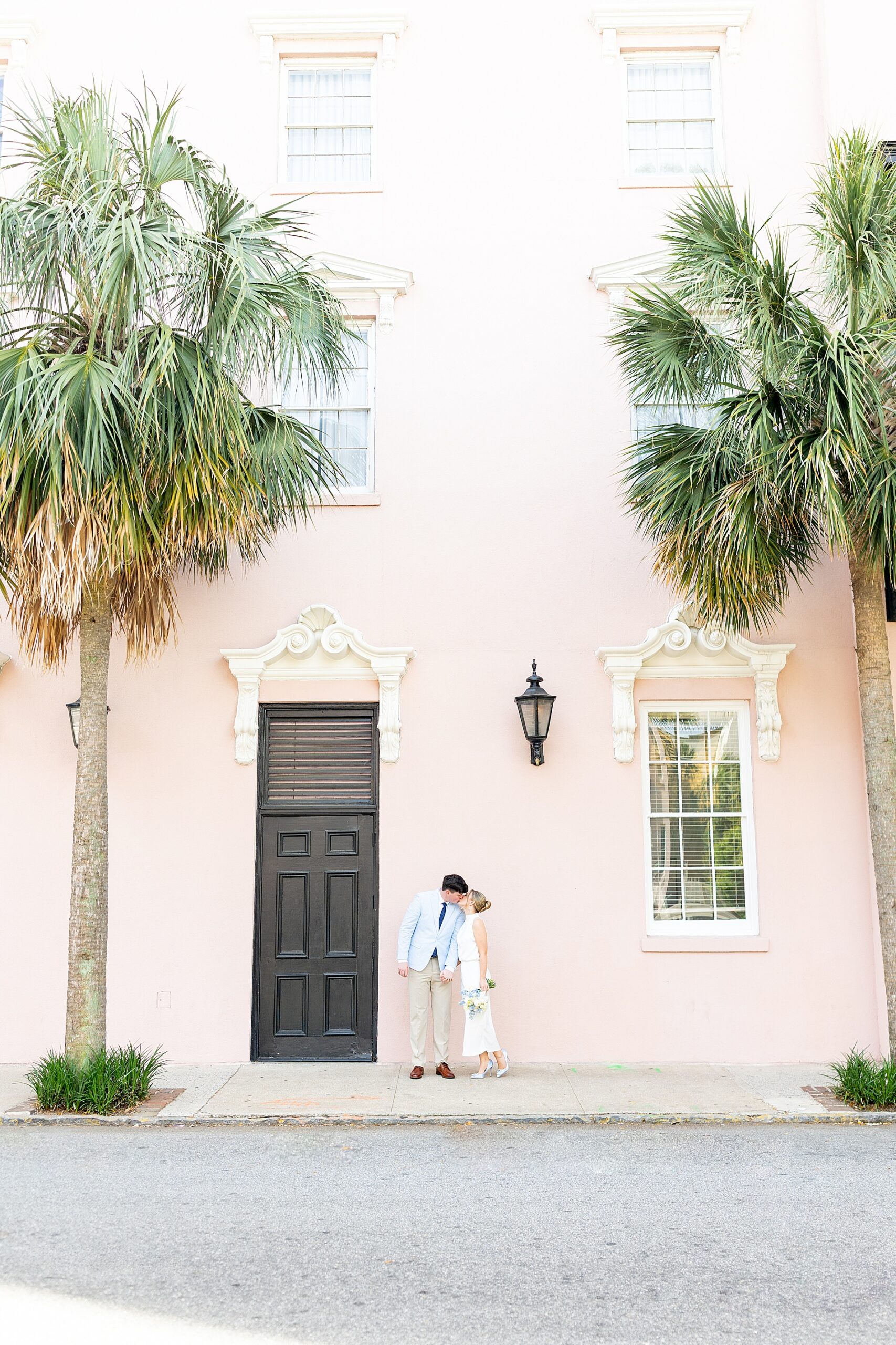 couple kiss in front of pastel pink building