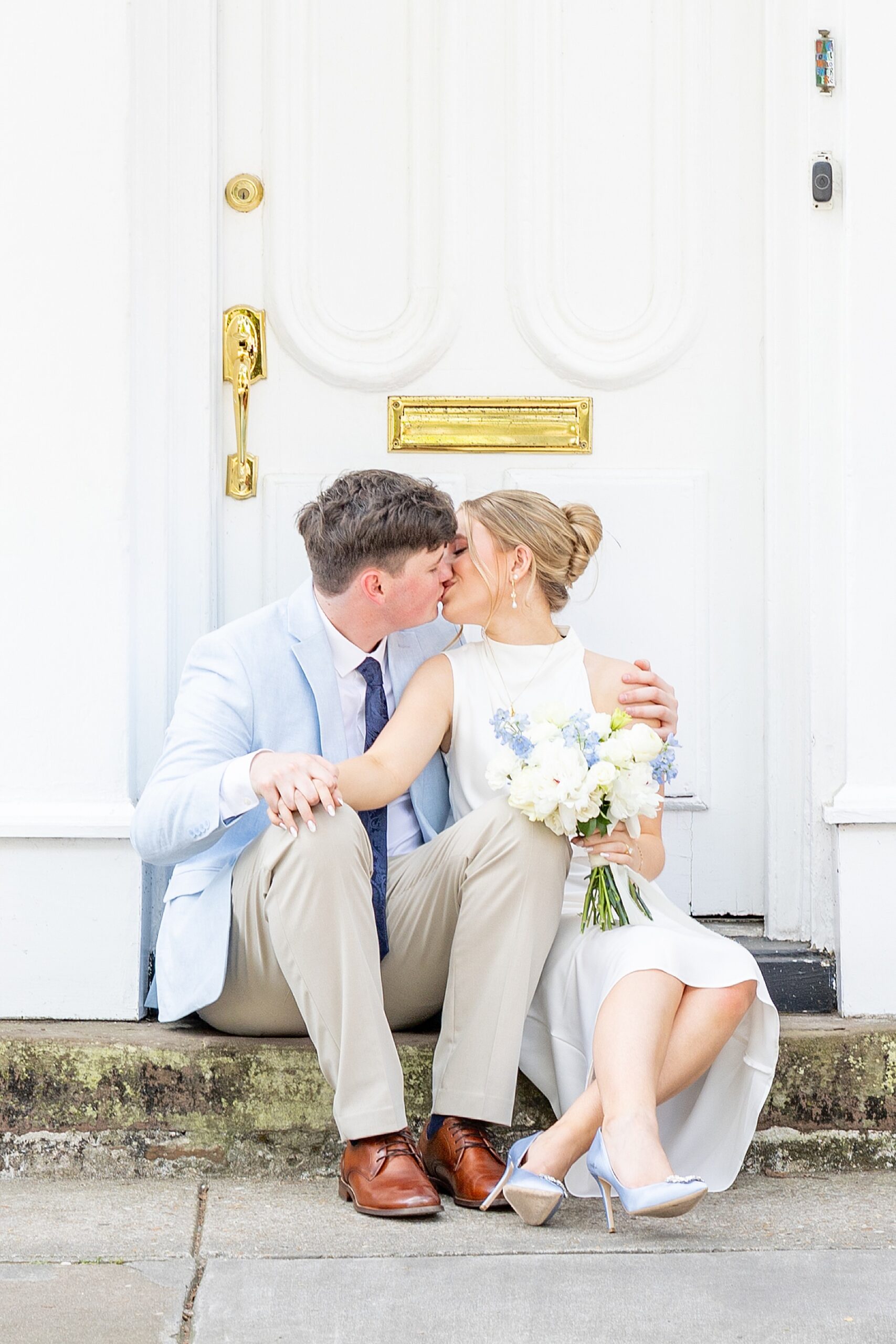 couple kiss as they sit on steps in front of house