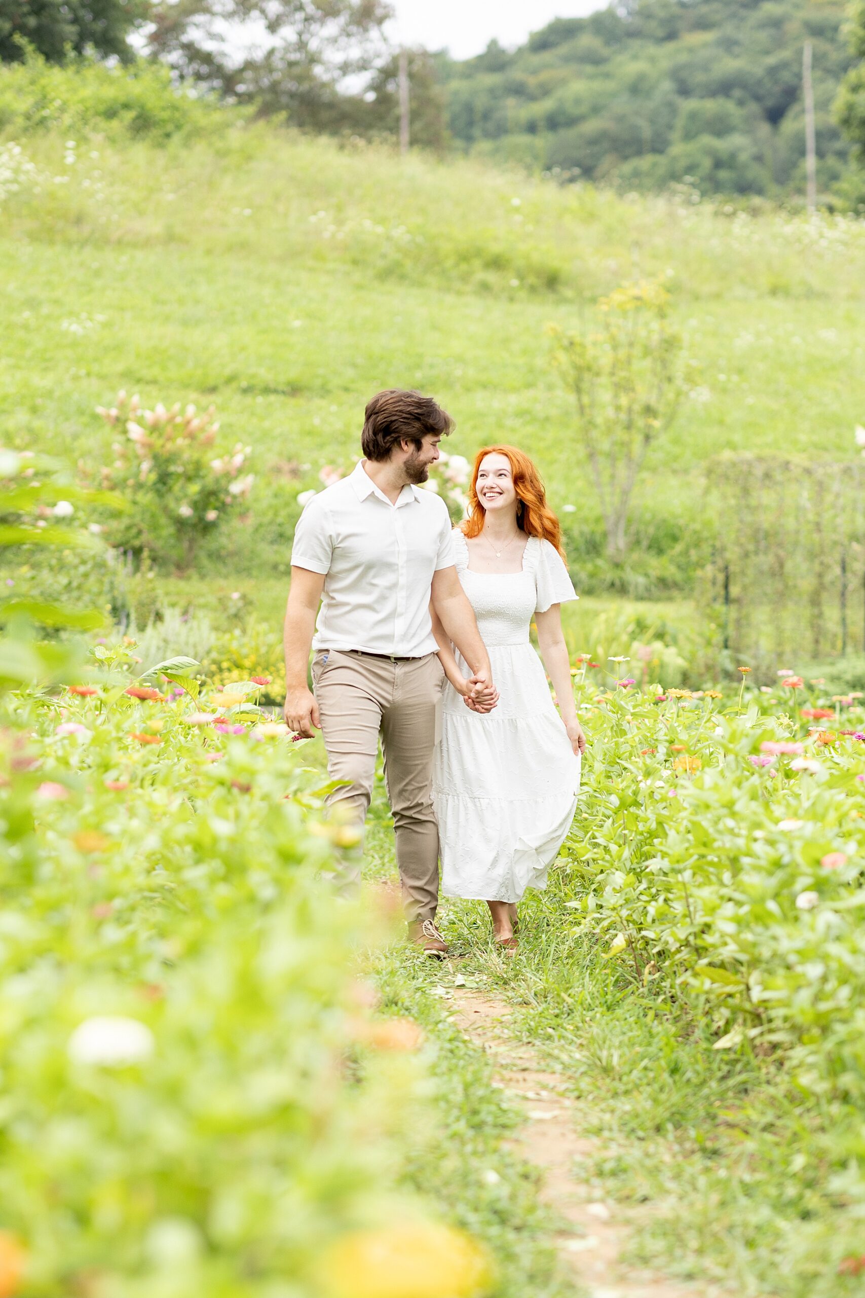 couple walk along path in field holding hands 