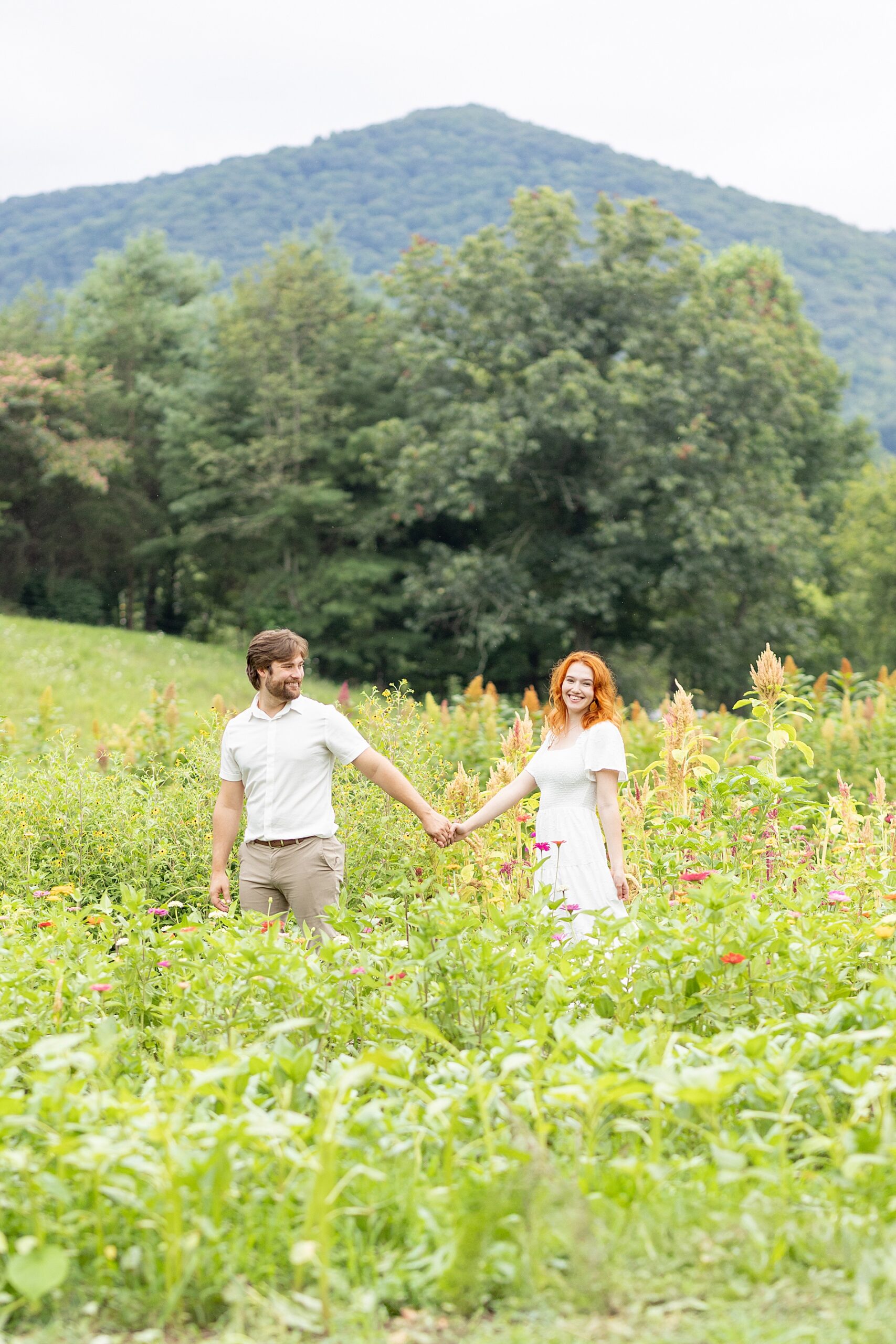 couple holding hands in field with Blue ridge Mountains in the distance