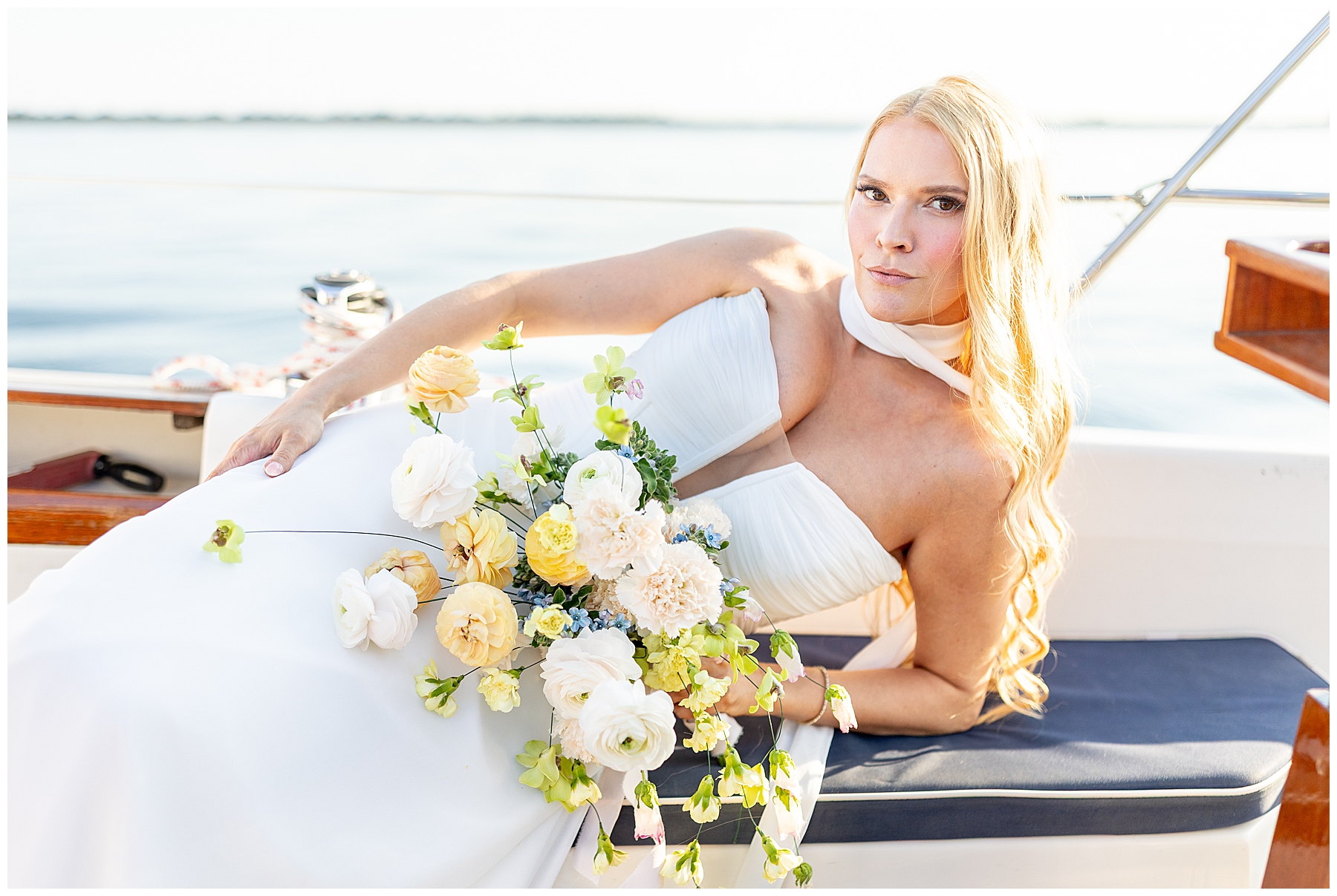 bride lays on sailboat holding organic white and yellow flowers