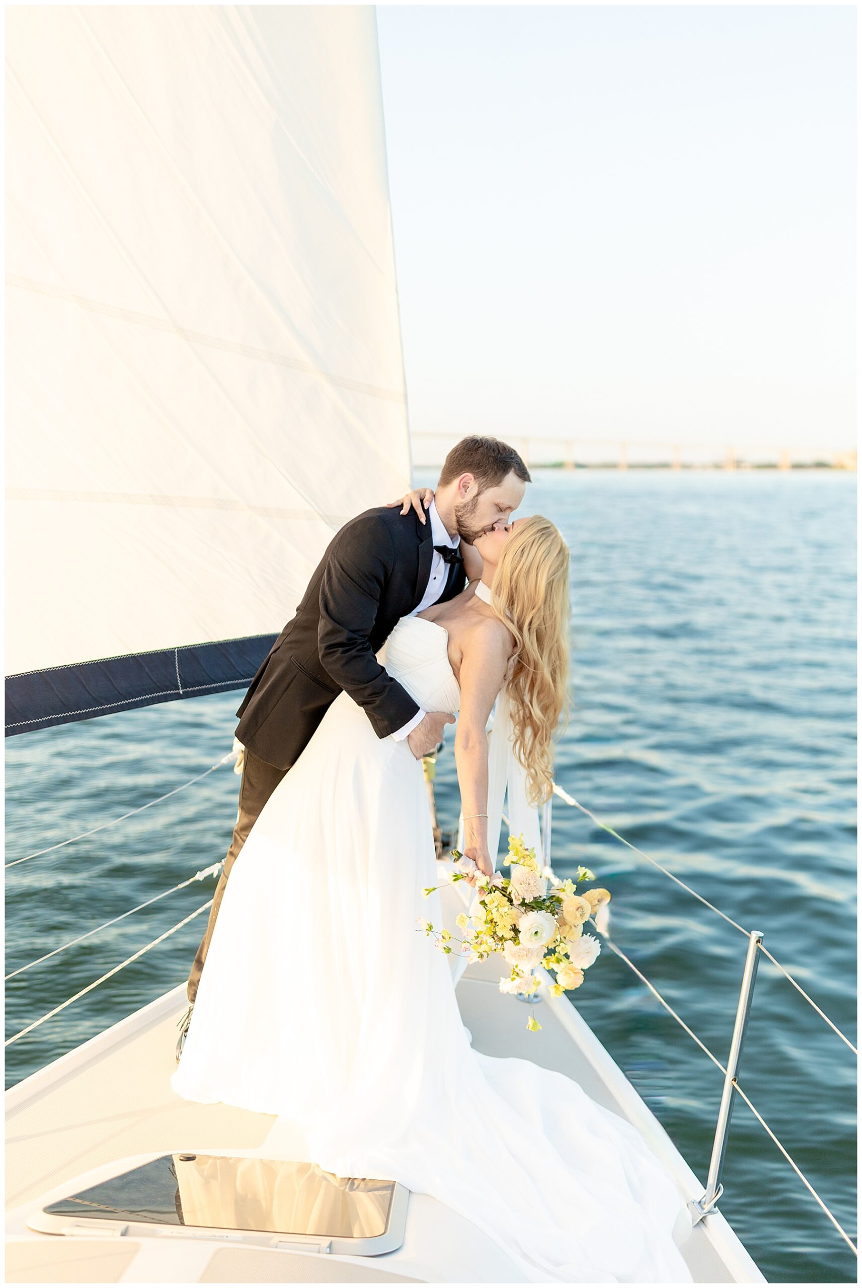 newlyweds kiss on a sailboat as it sails on the water of charleston harbor 