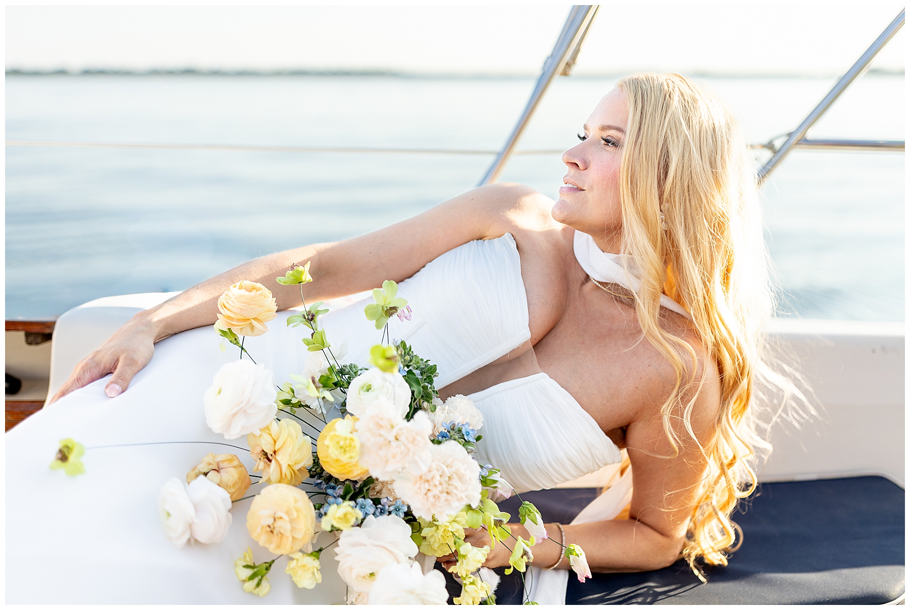 bride lays on her side holding bridal bouquet of soft yellow and white flowers 