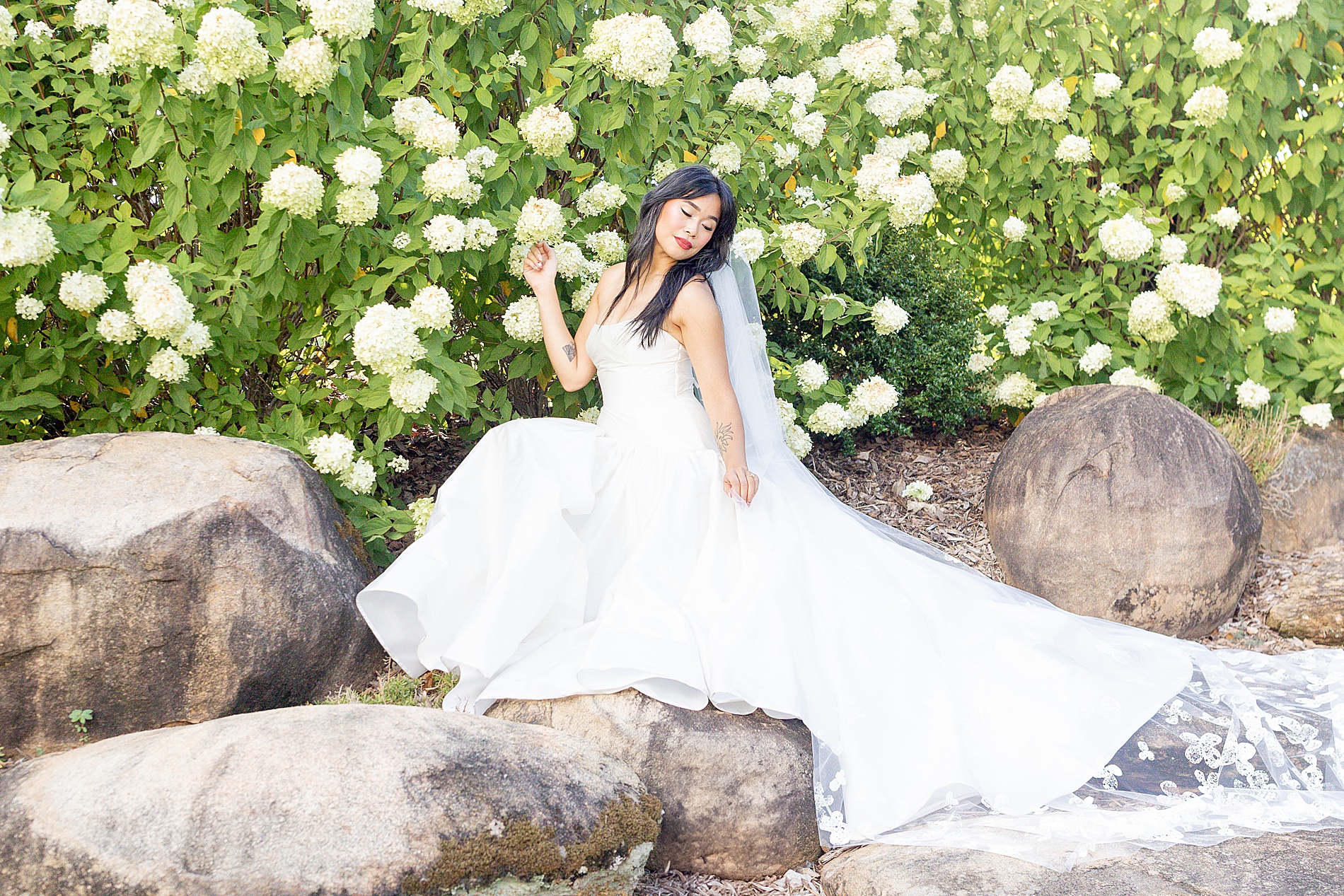 bride sits on rocks by white blooms 