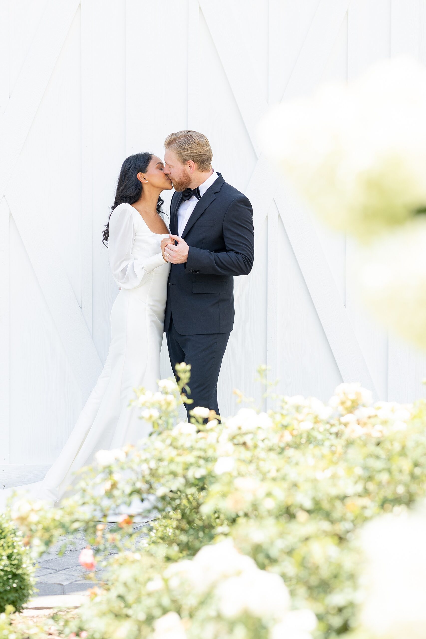 bride and groom kiss with soft summer flowers surrounding them