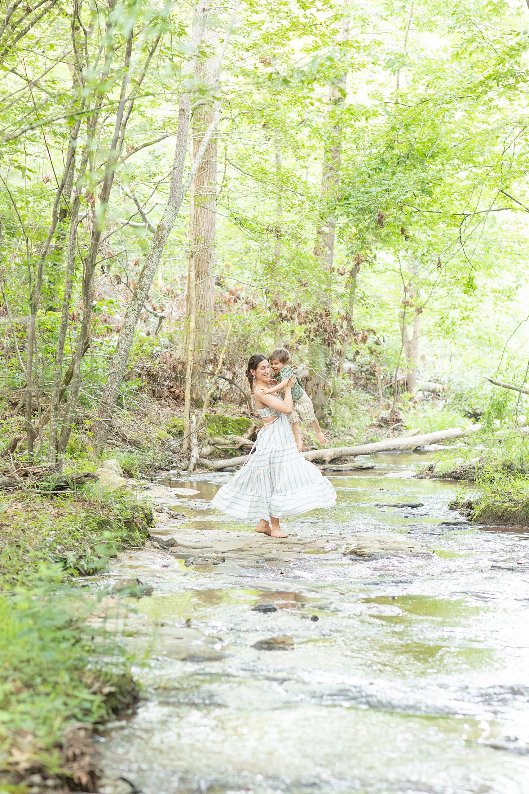 mother twirls around with her son in creekbed