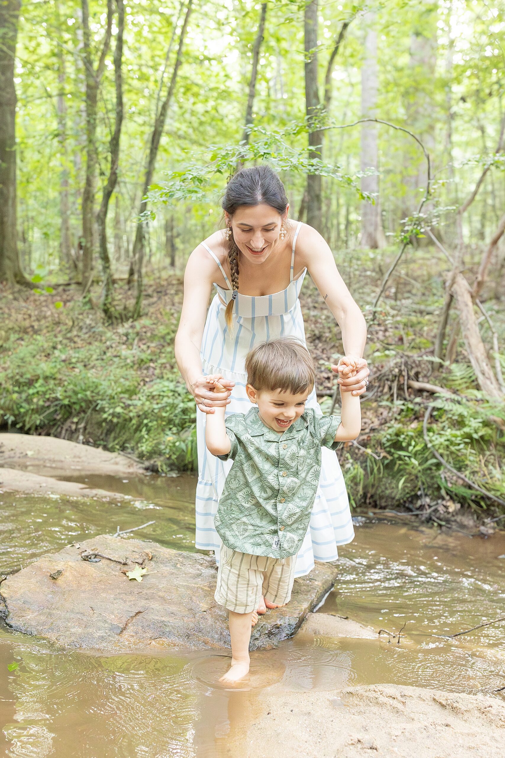 mom helping son walk across rocks in creek