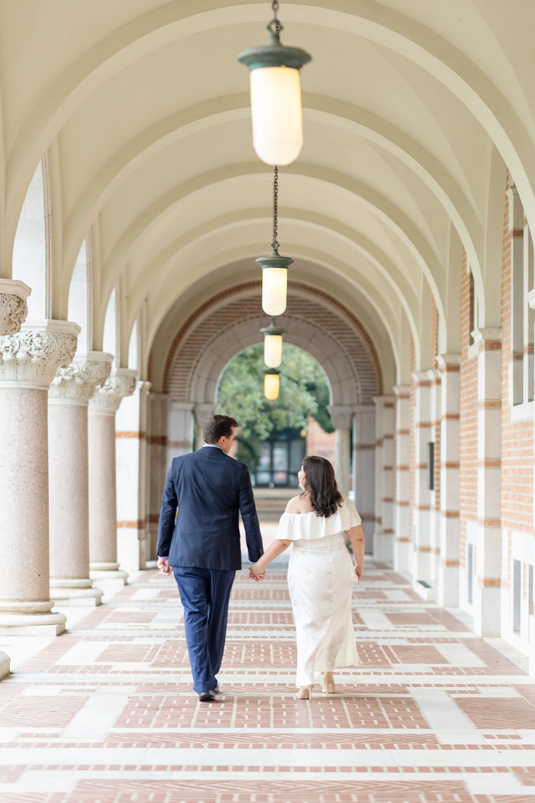 engaged couple walk down arched hallway at Rice University