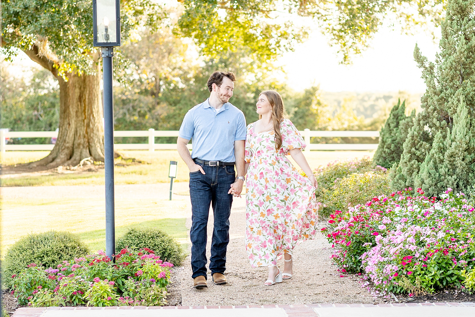 couple hold hands and walk along flower lined path
