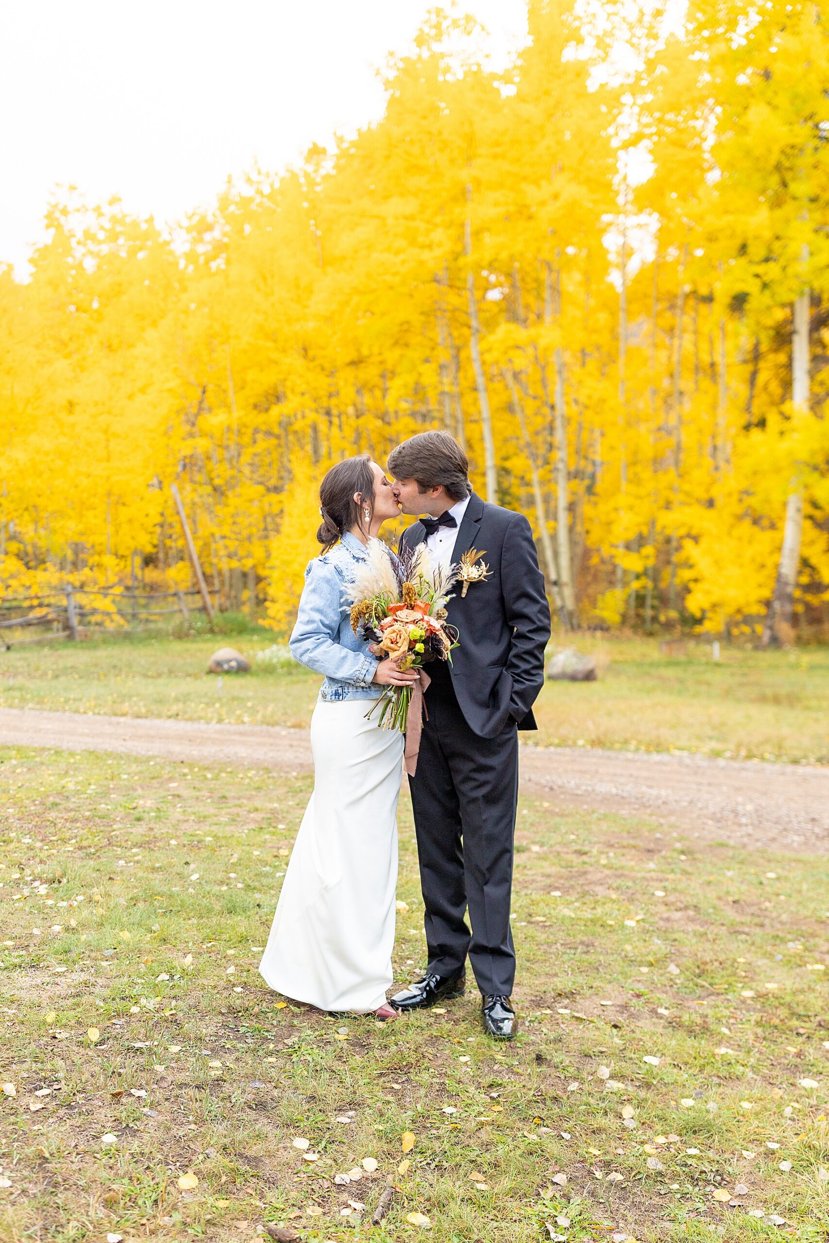 couple kiss in front of vibrant fall trees