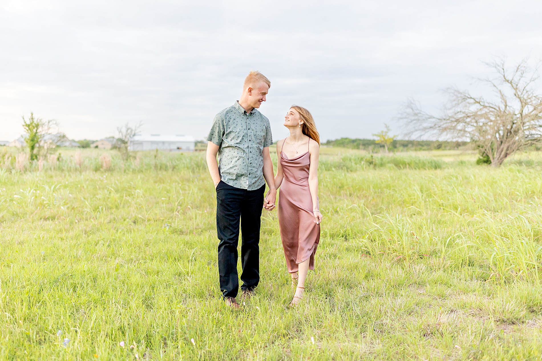 engaged couple walk through field together holding hands