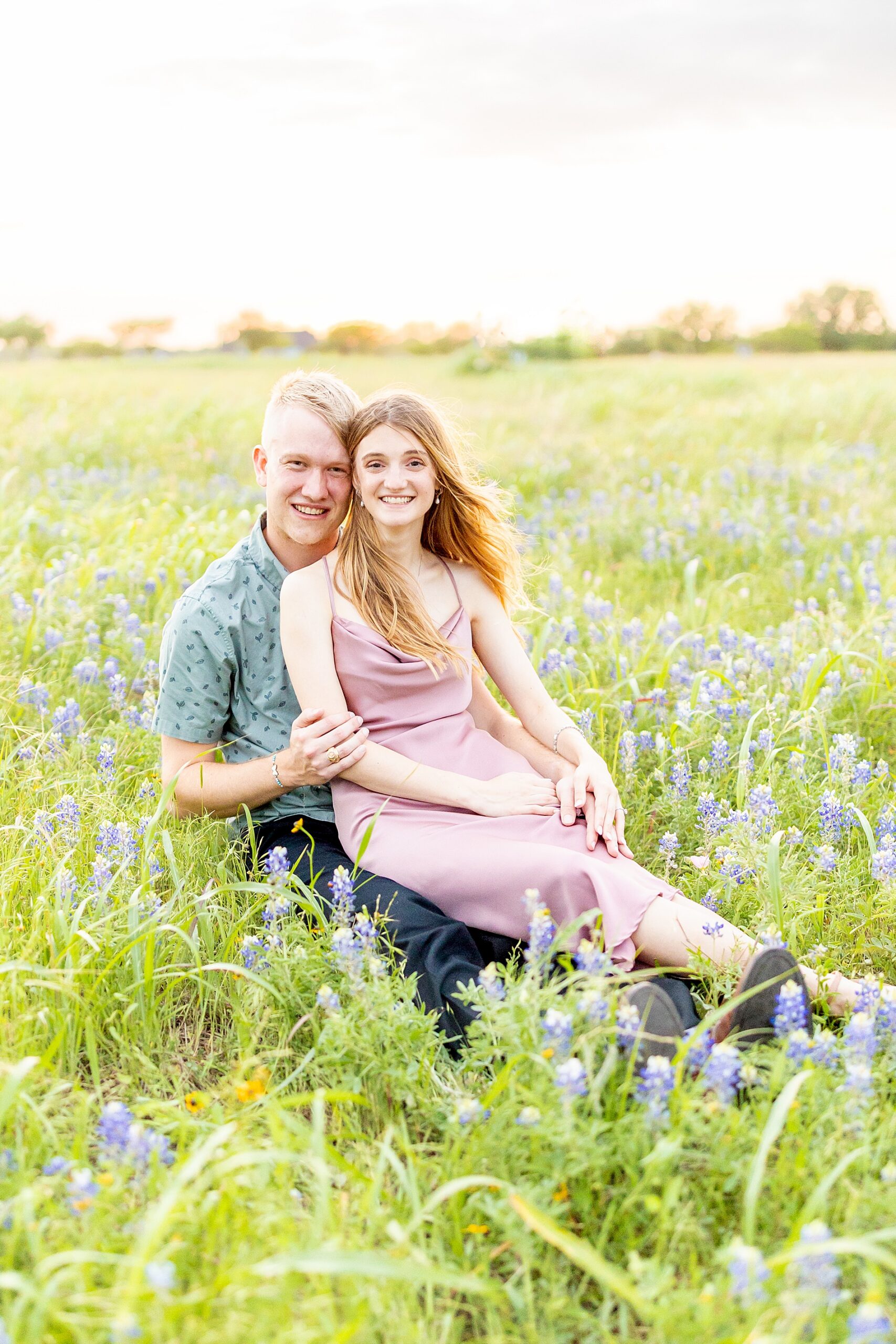 engaged couple sit in field of bluebonnets